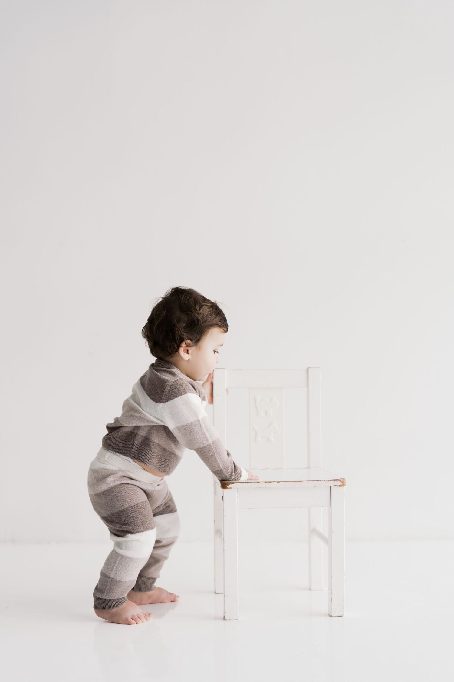 A young child sits on a chair against a plain white background.