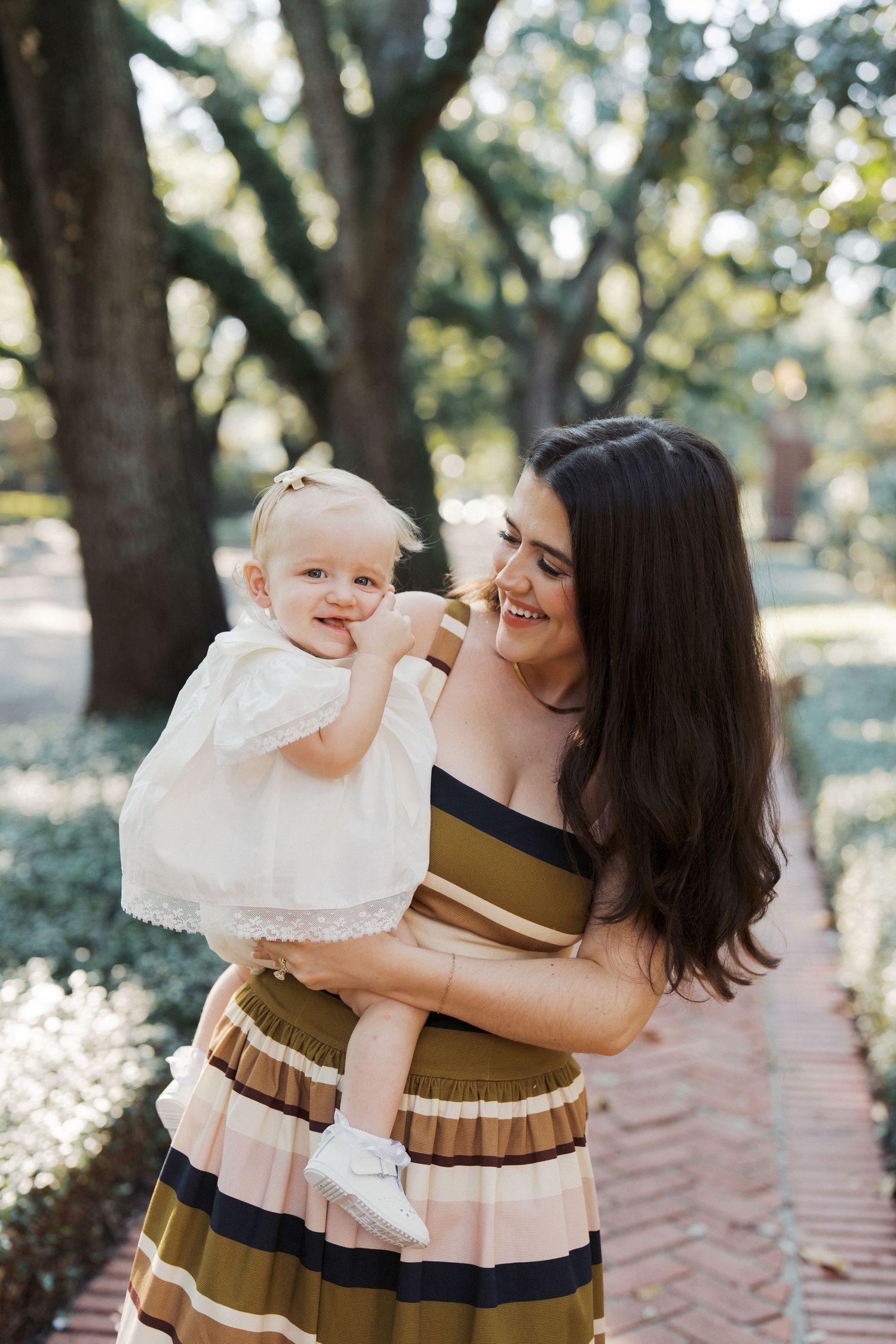 A sweet candid moment captured in a park setting with soft natural lighting and matching brown striped dresses.