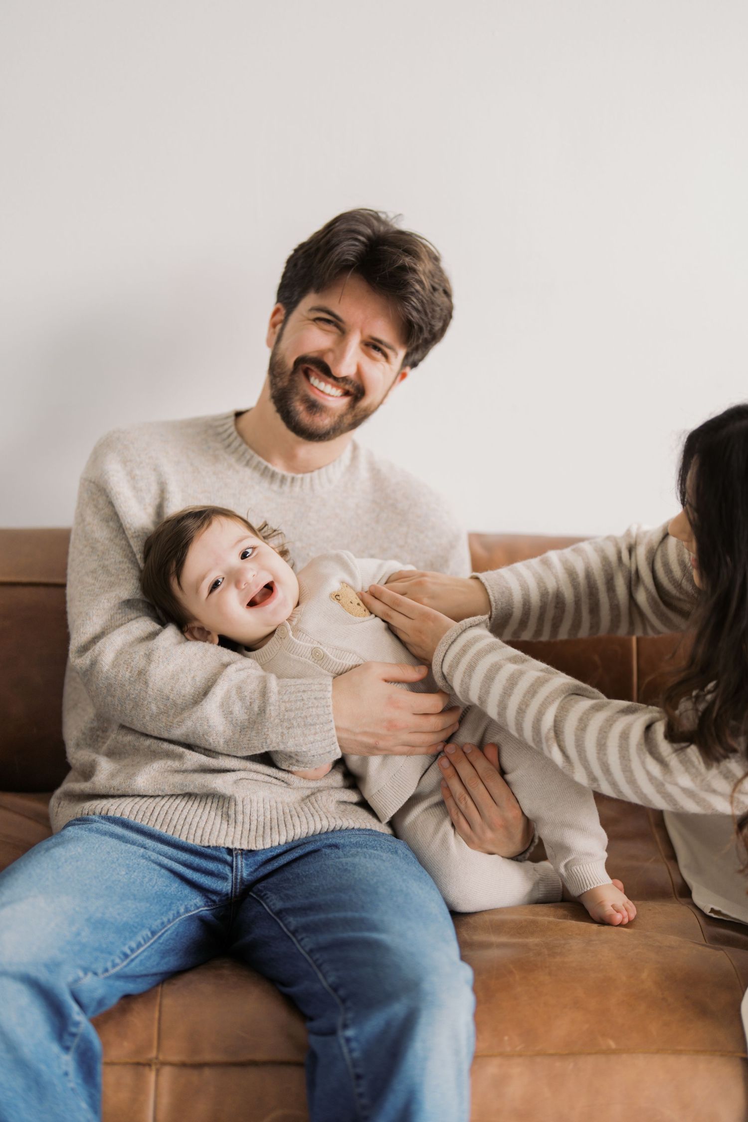 A man sitting on a couch and holding a smiling baby.
