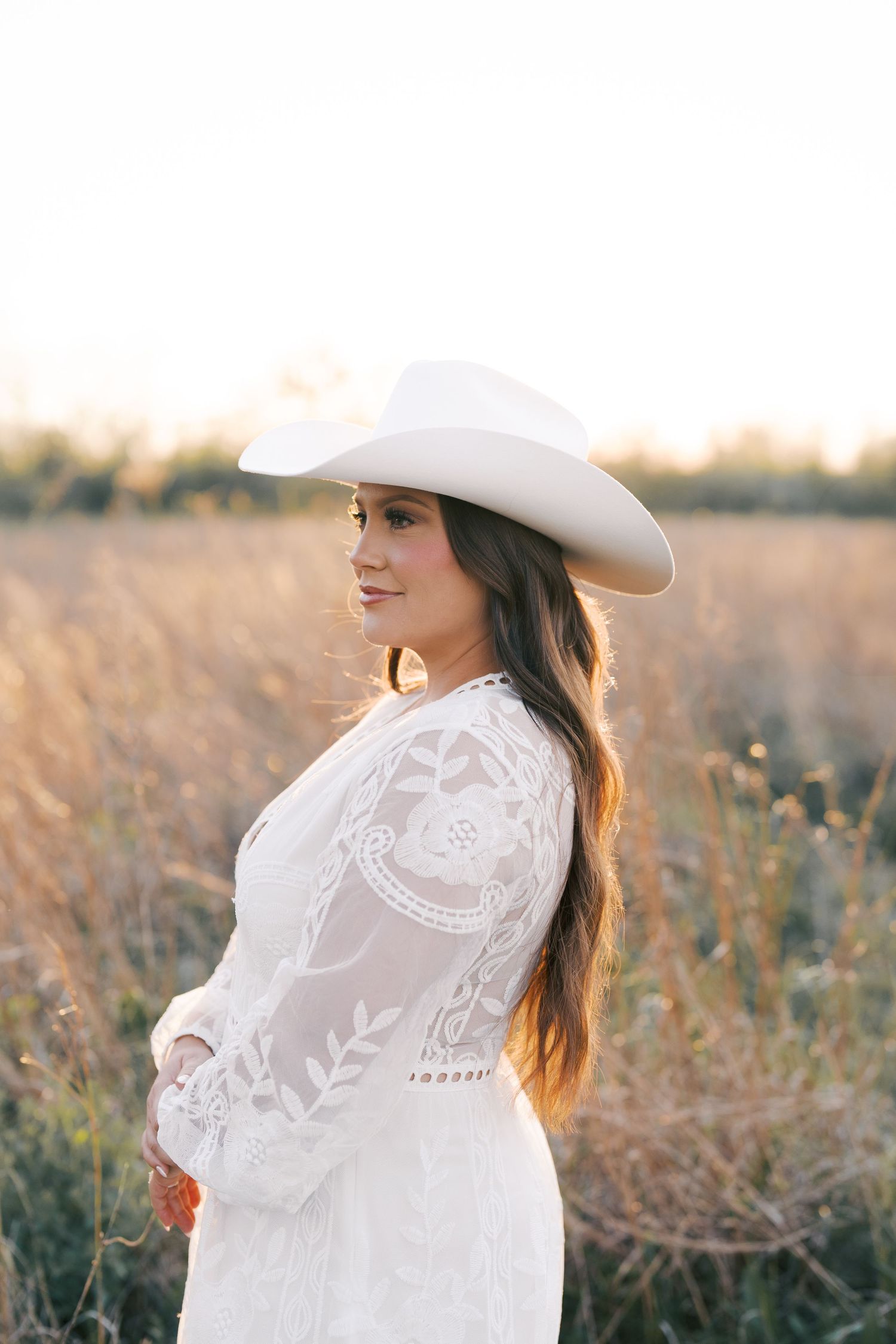 Dreamy golden hour portrait in a field wearing white lace dress and western hat.