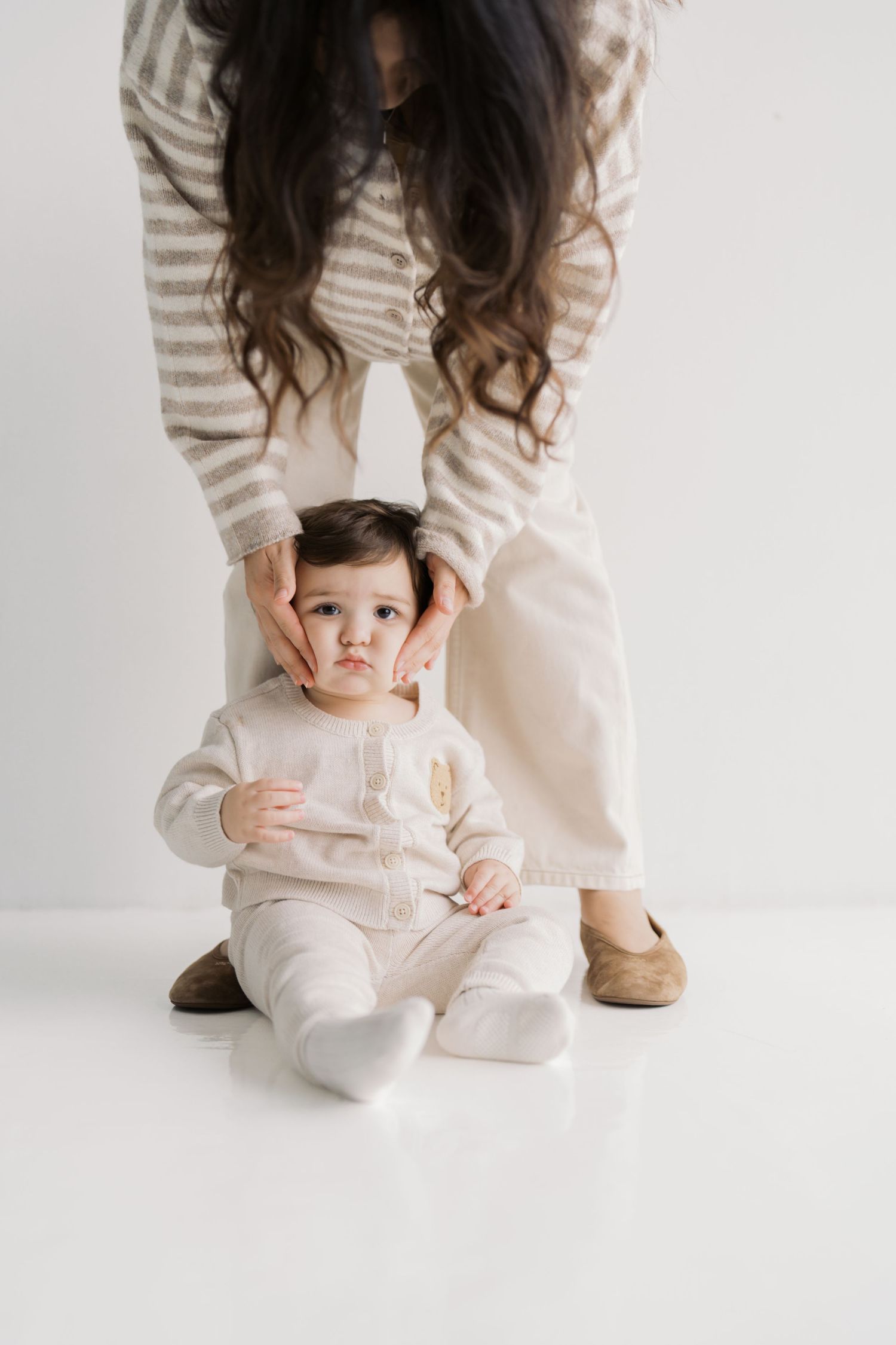 A young child sitting on the floor, surrounded by a woman in a striped sweater.