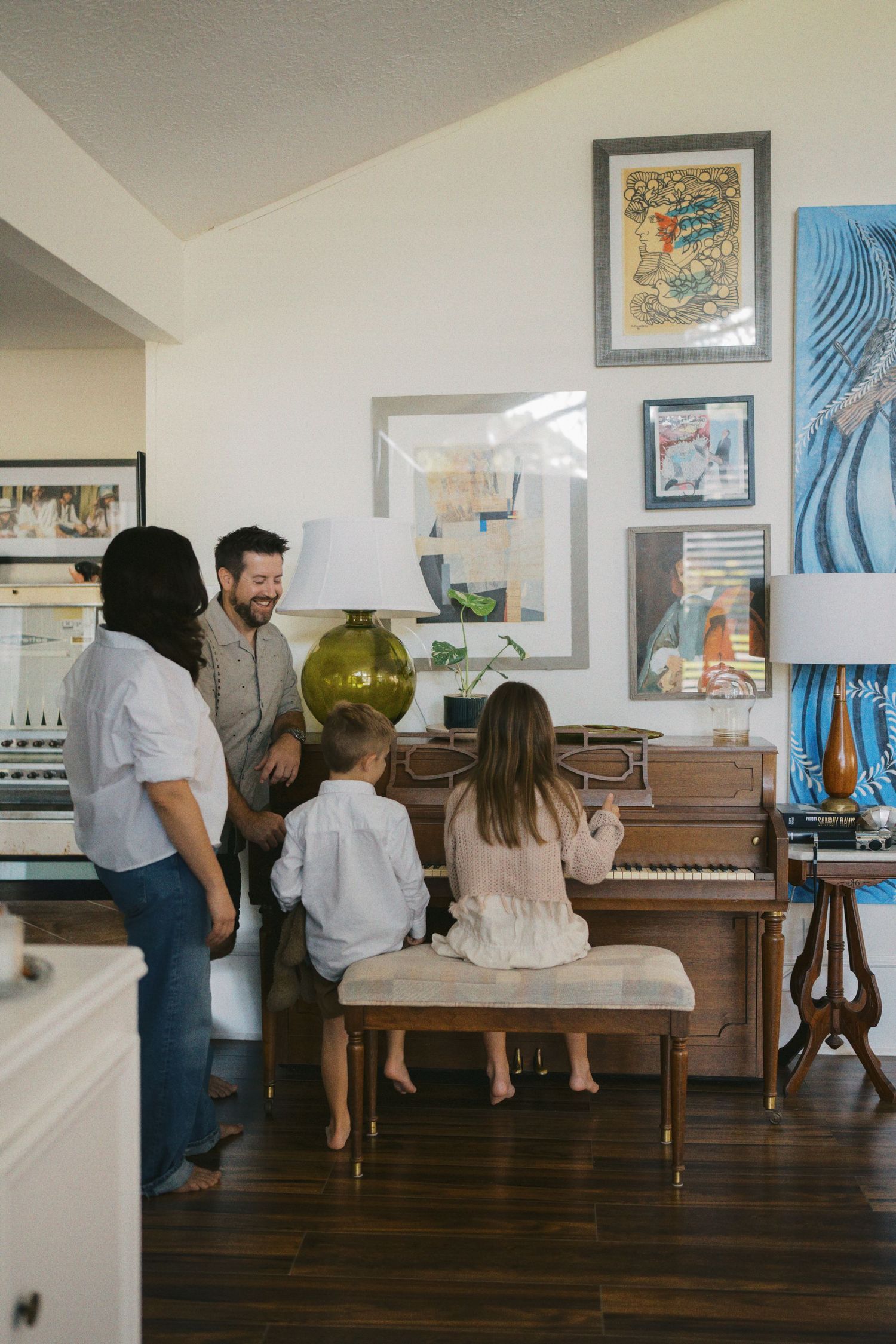 Family gathered around an upright piano in a cozy home with eclectic gallery wall art.