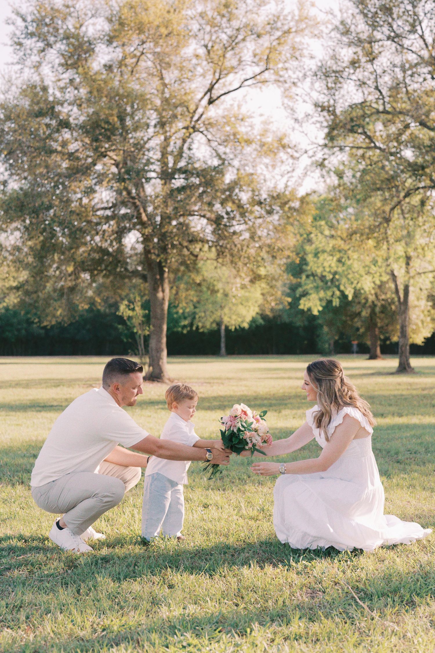 Family having fun falling backwards together in sequence on grassy field during golden hour sunset.
