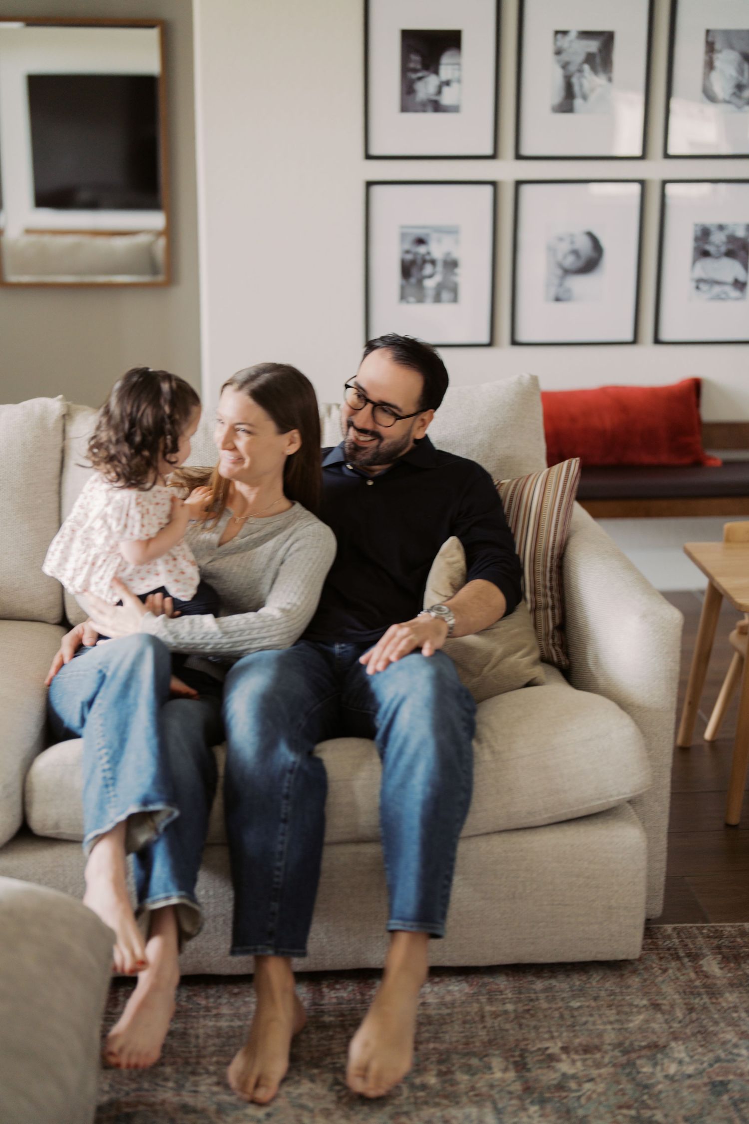 A family of three, including a mother, father, and young child, sitting together on a couch in a cozy living room.