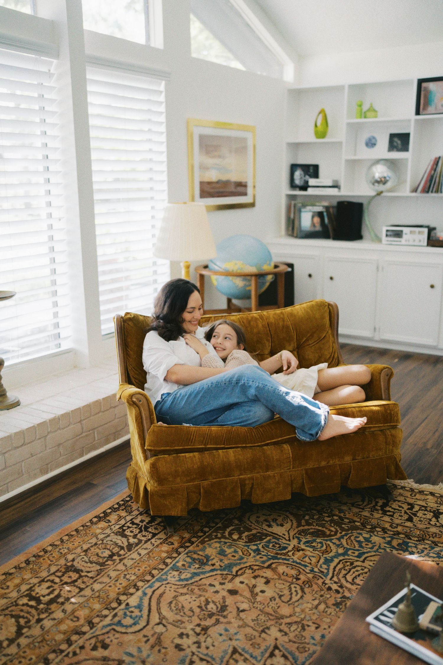 Mother and child cuddling together on a golden velvet armchair in a cozy living room with hardwood floors.