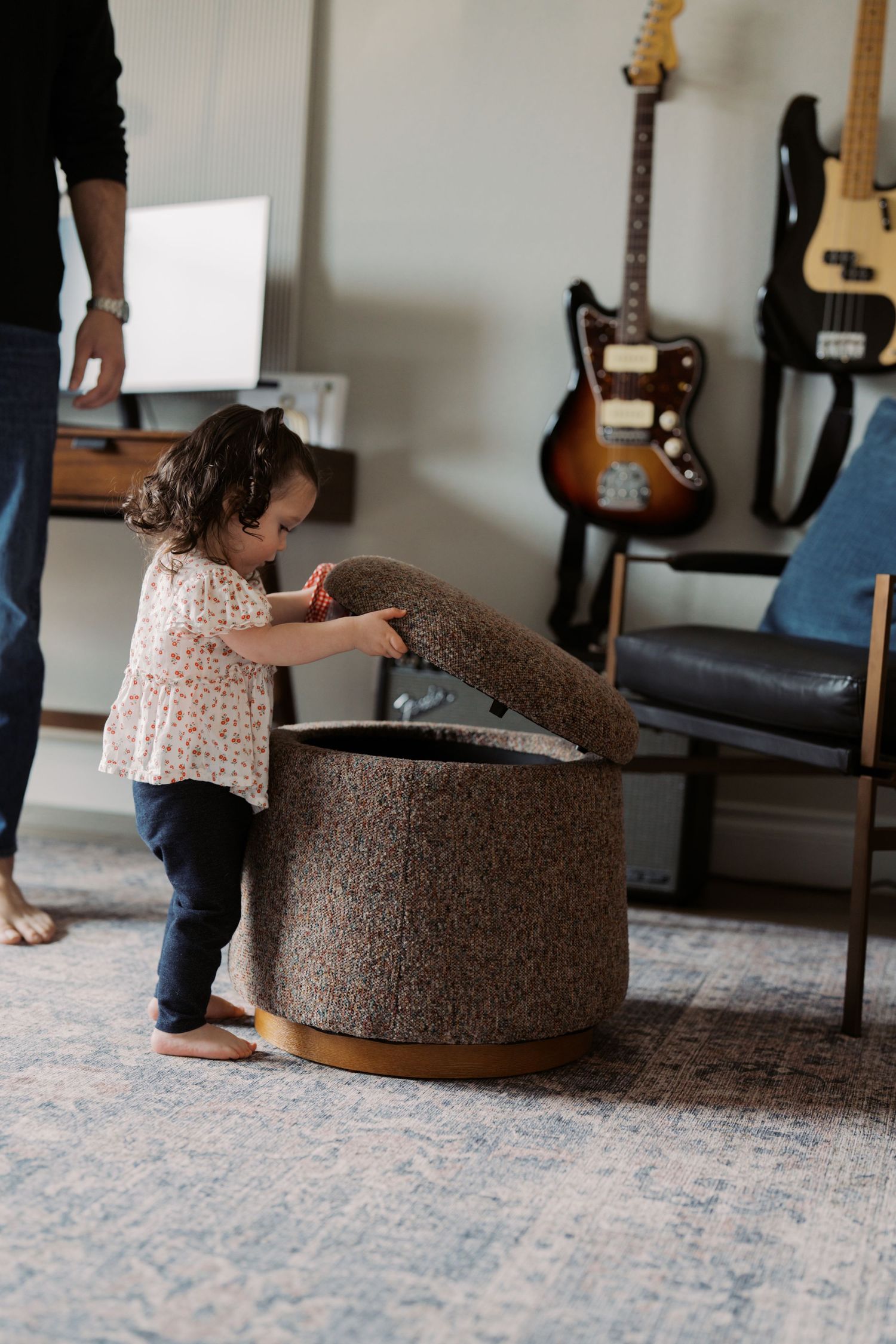 A young girl sits on a round, cushioned chair in a room with musical instruments in the background.