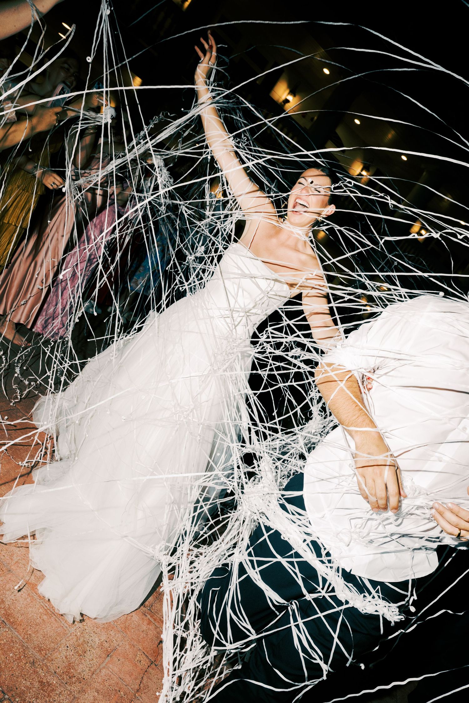 Happy couple dances and celebrates at a wedding reception with white streamers against a dark background.