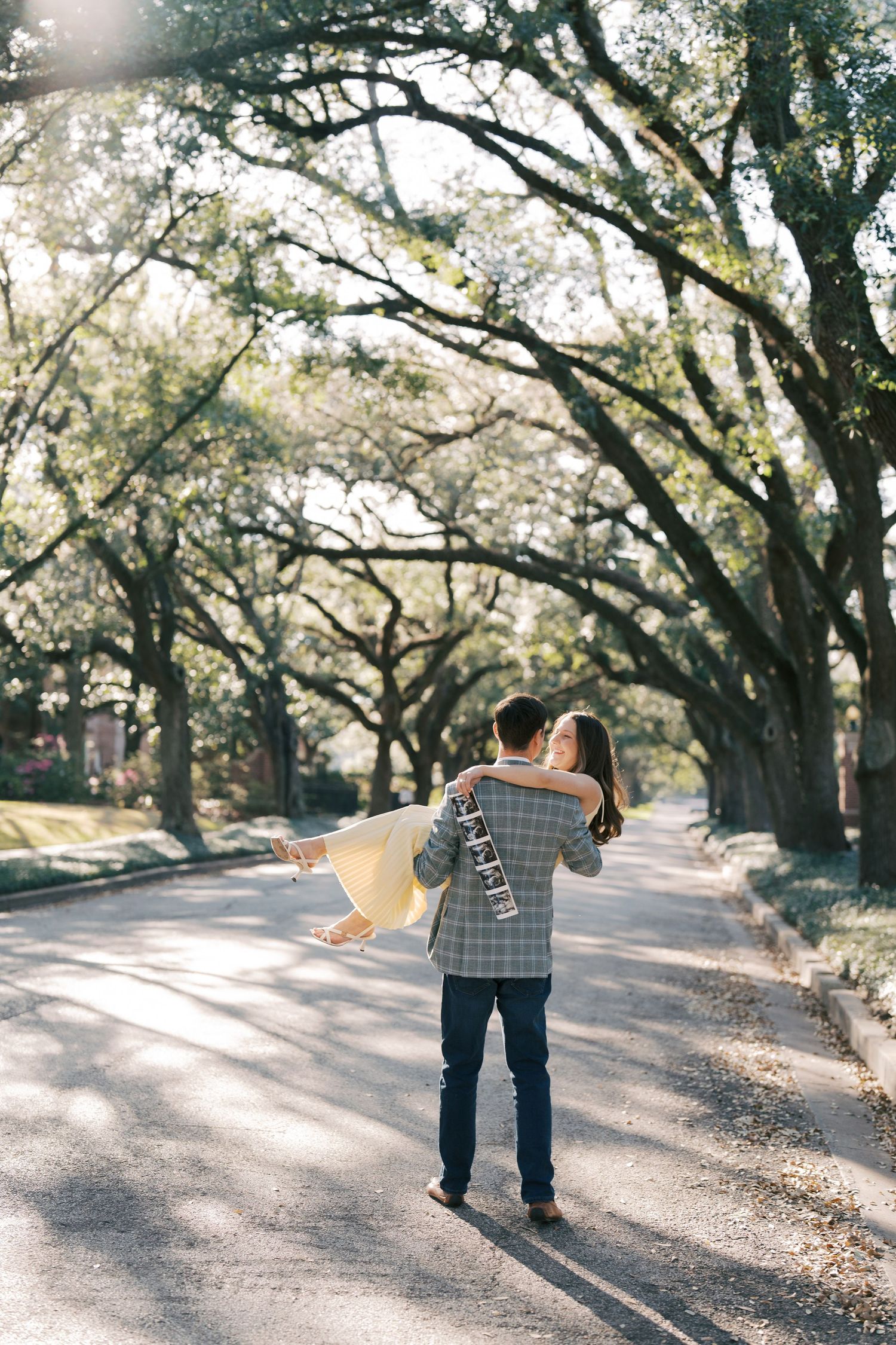 A person walking down a path surrounded by lush, overarching trees in a park or garden setting.