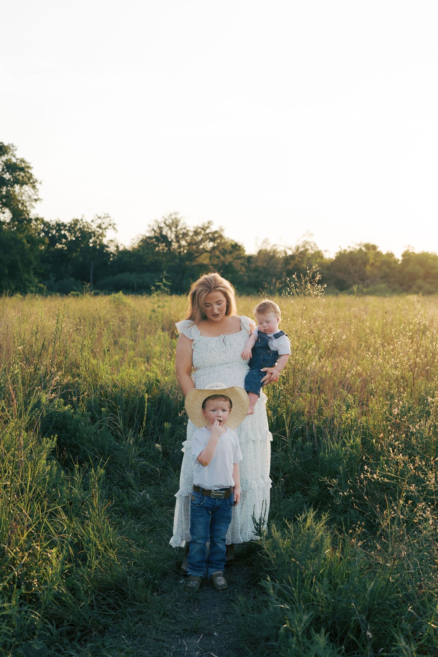 Three photos show people playing and embracing in a golden field at sunset with tall wildflowers and grasses.
