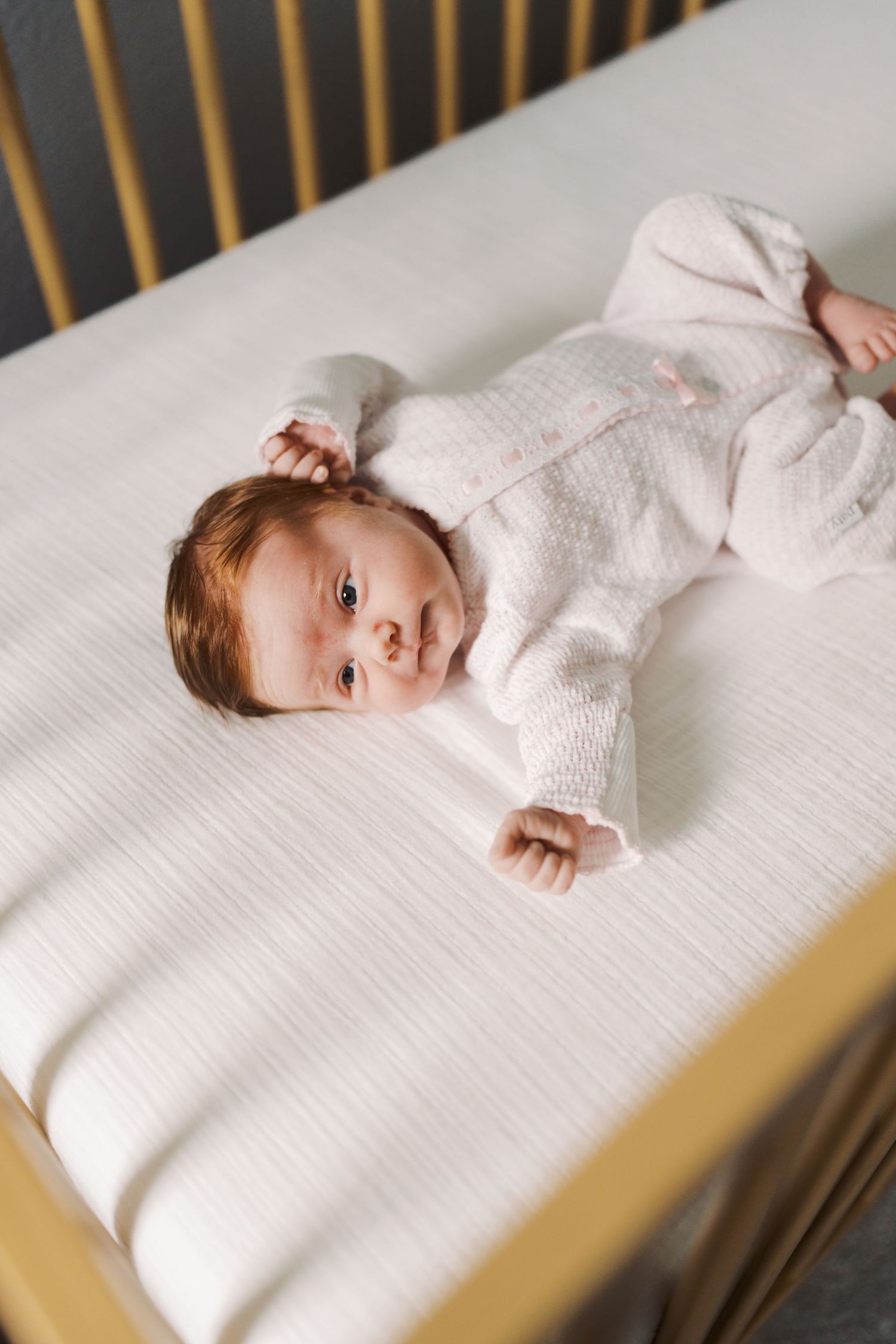 A newborn baby lies peacefully in a crib, wrapped in a soft white blanket.