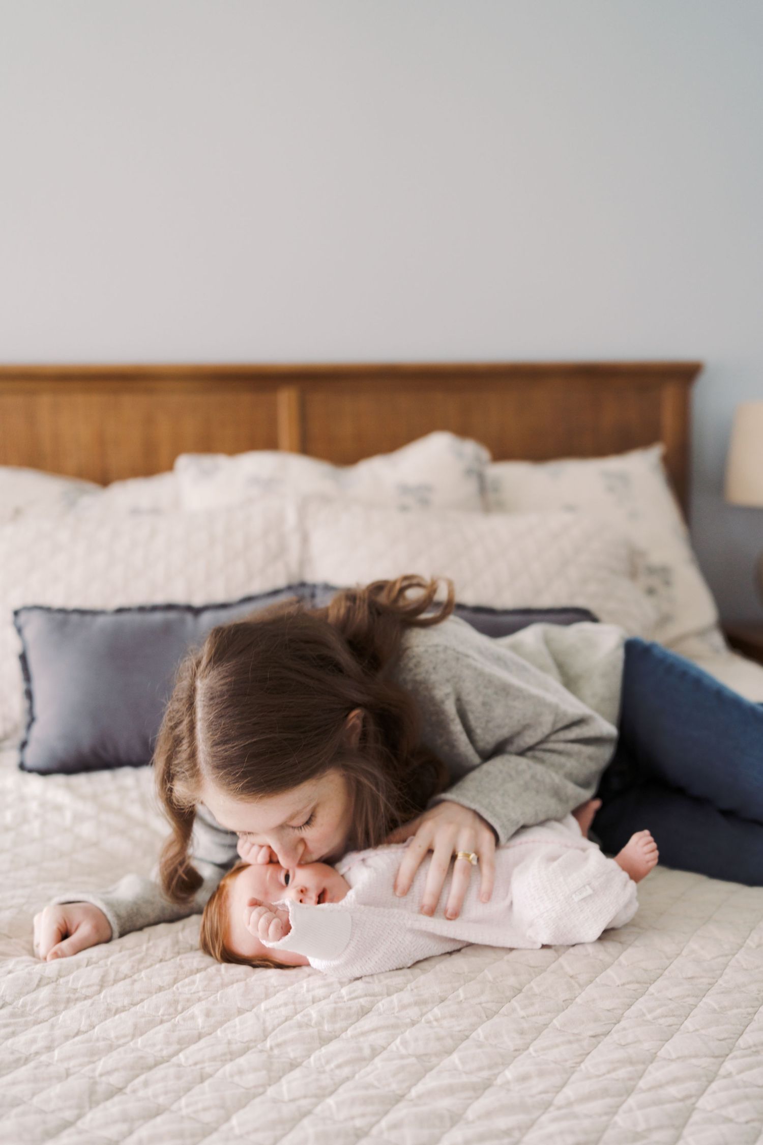 A woman lies on a bed, tenderly embracing a baby in a cozy, domestic scene.