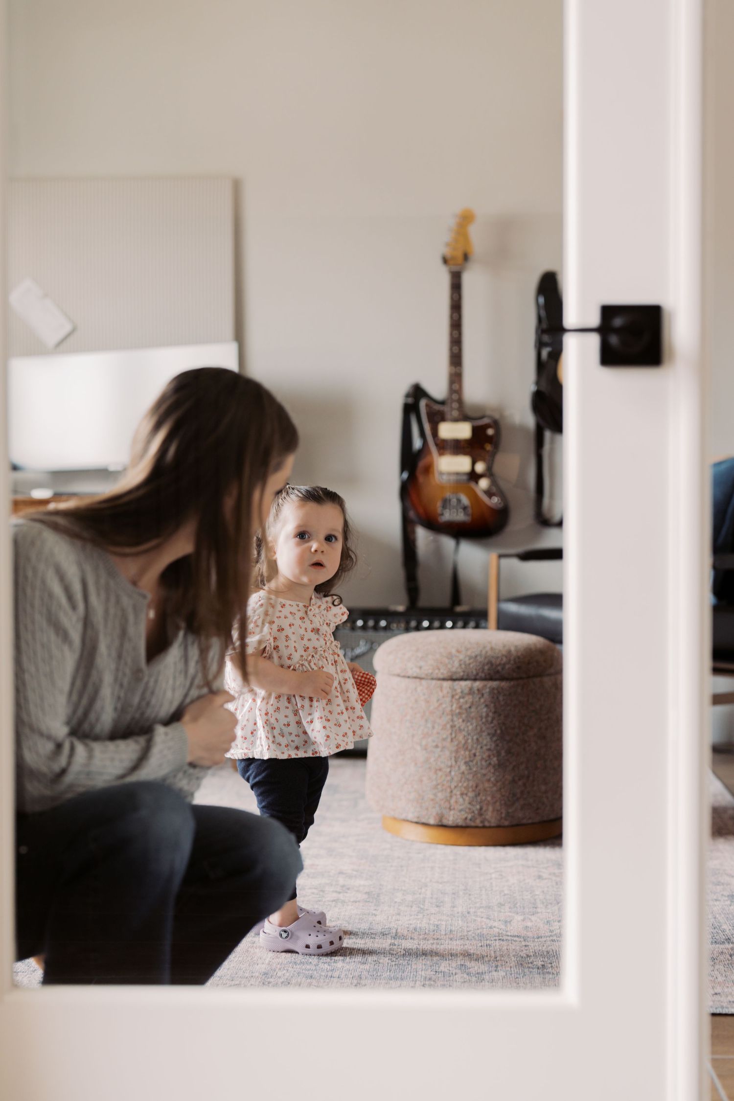A woman sits on a couch, playing with a young child in a cozy living room setting with a guitar and other decor.