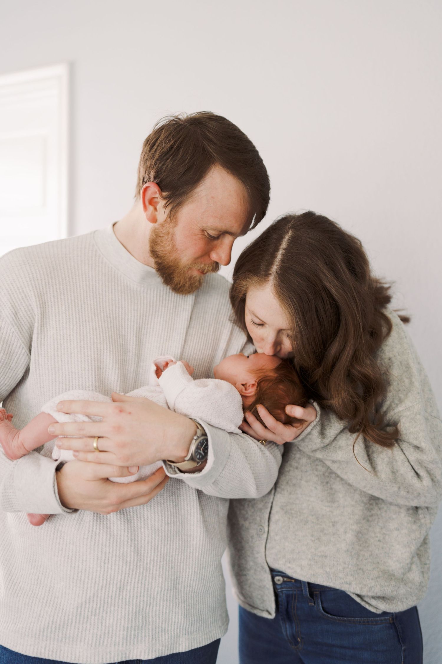 A man and a woman are embracing and holding a newborn baby, displaying a tender family moment.