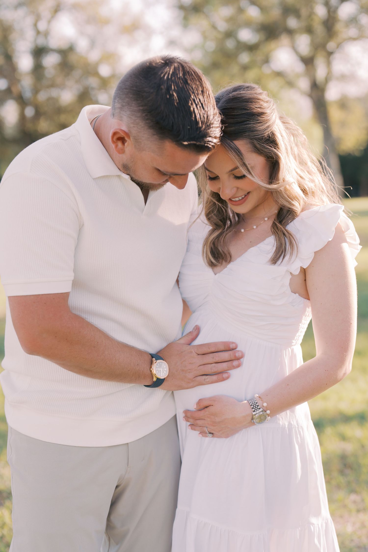 A couple in white clothing embraces tenderly in a sun-lit outdoor setting during a romantic photoshoot.