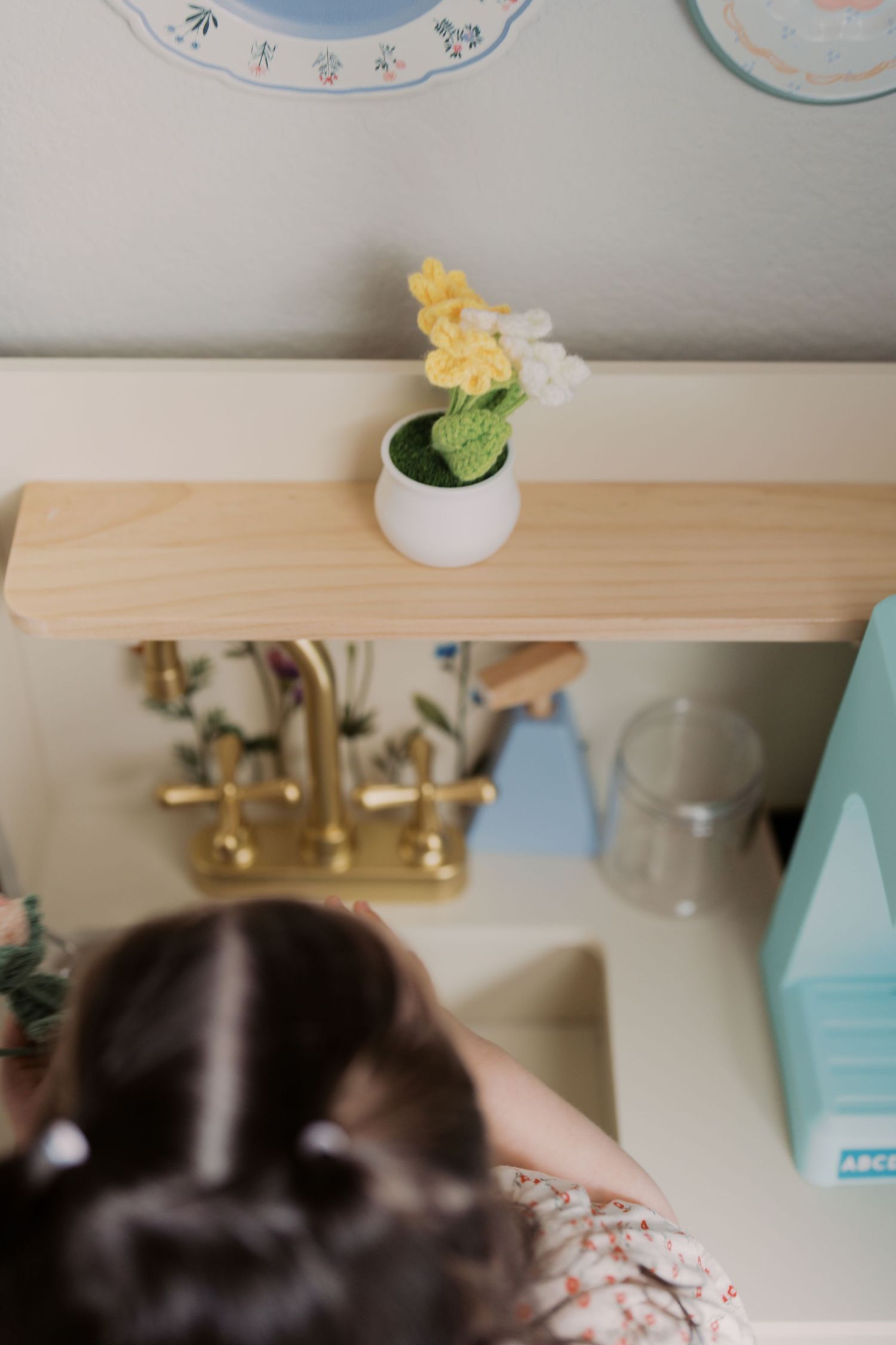 The image shows a small potted plant with yellow flowers on a wooden shelf, with a mirror and other decor visible in the background.