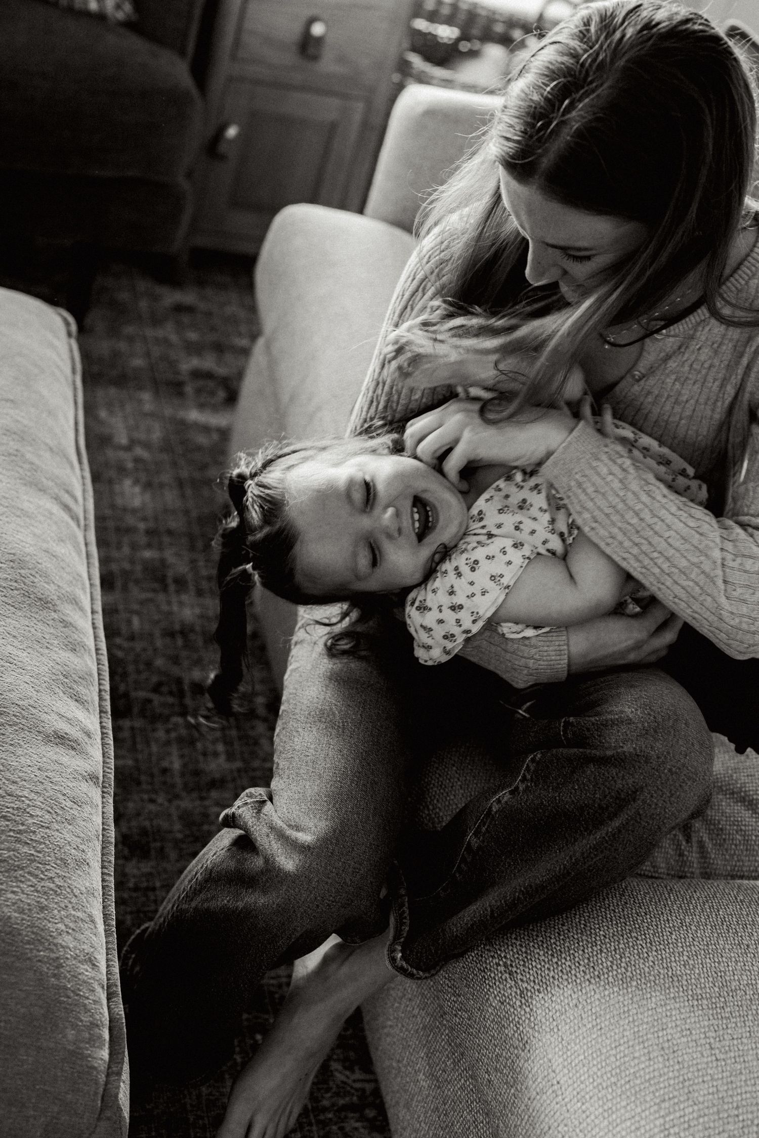 A tender black and white moment showing parent and child laughing together on a couch.
