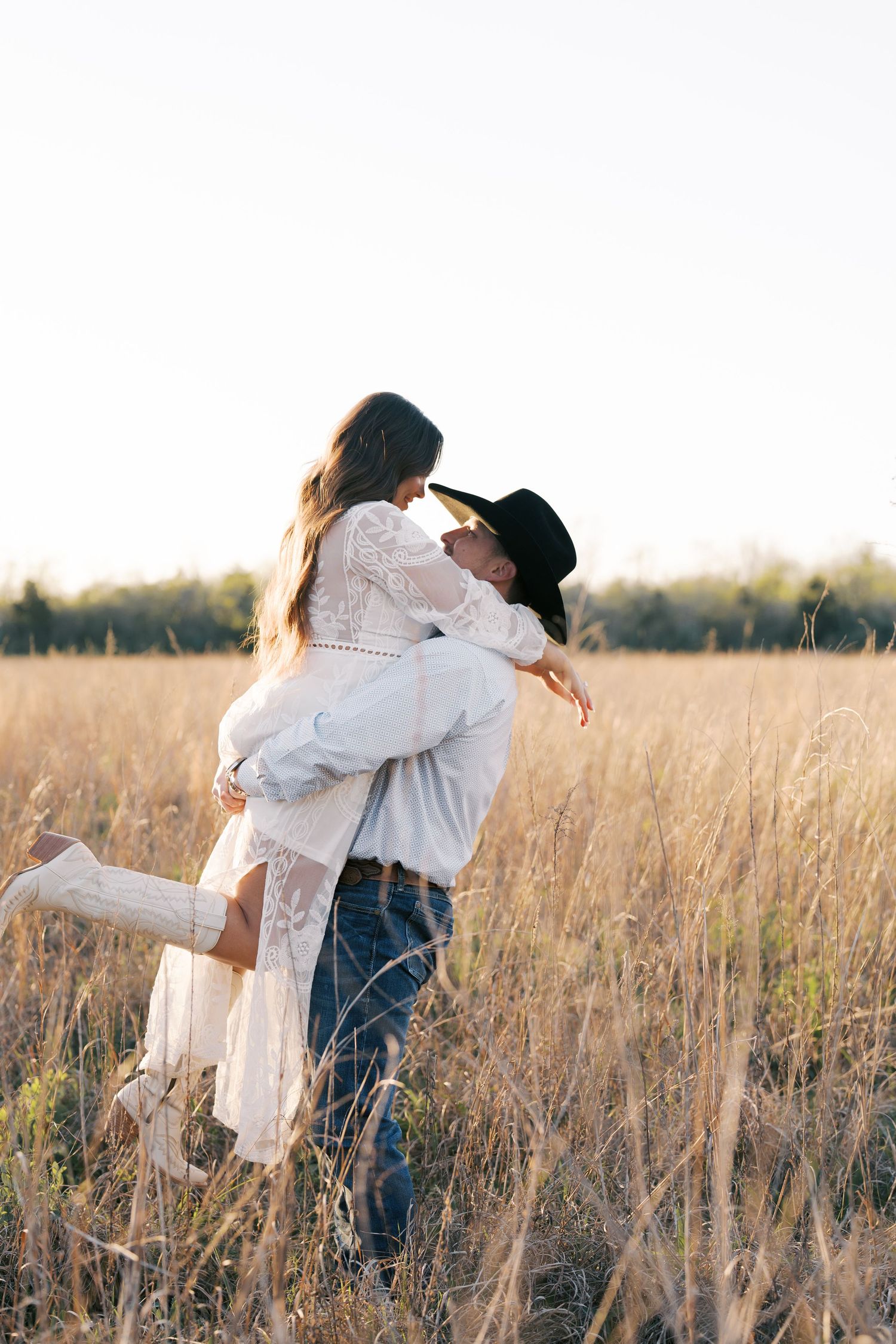 Couple embracing in tall grass field during golden hour sunset.