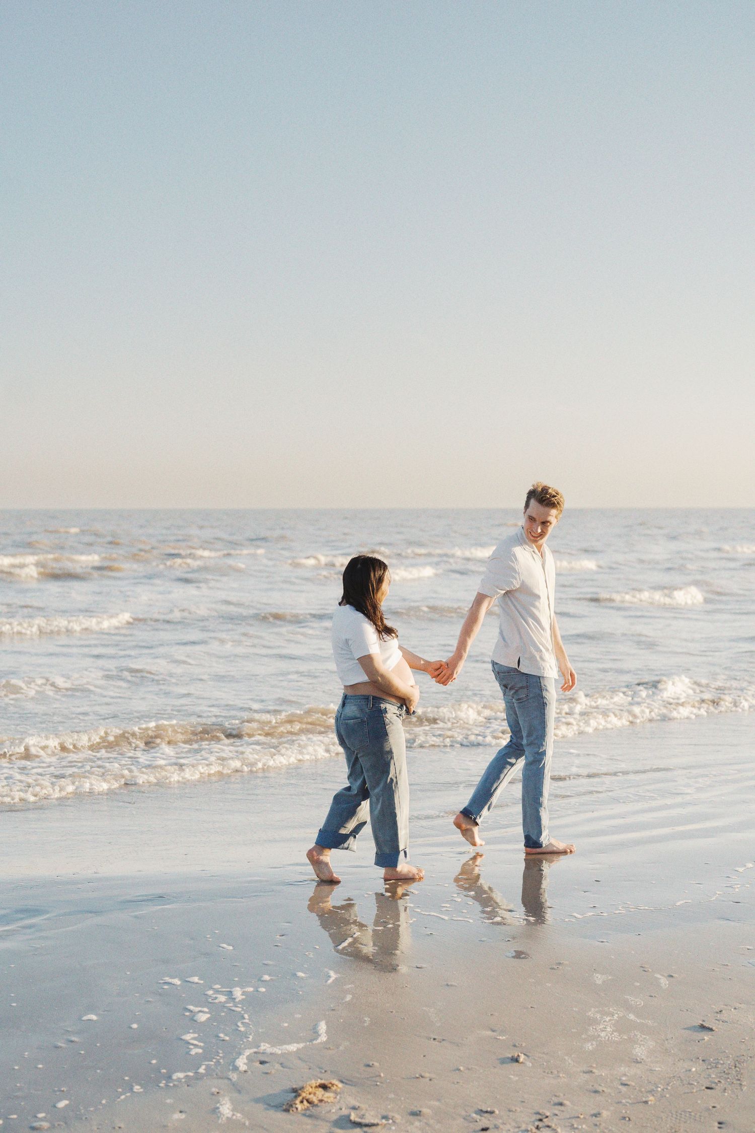 Two people, a man and a woman, walking hand-in-hand on the beach near the ocean waves.