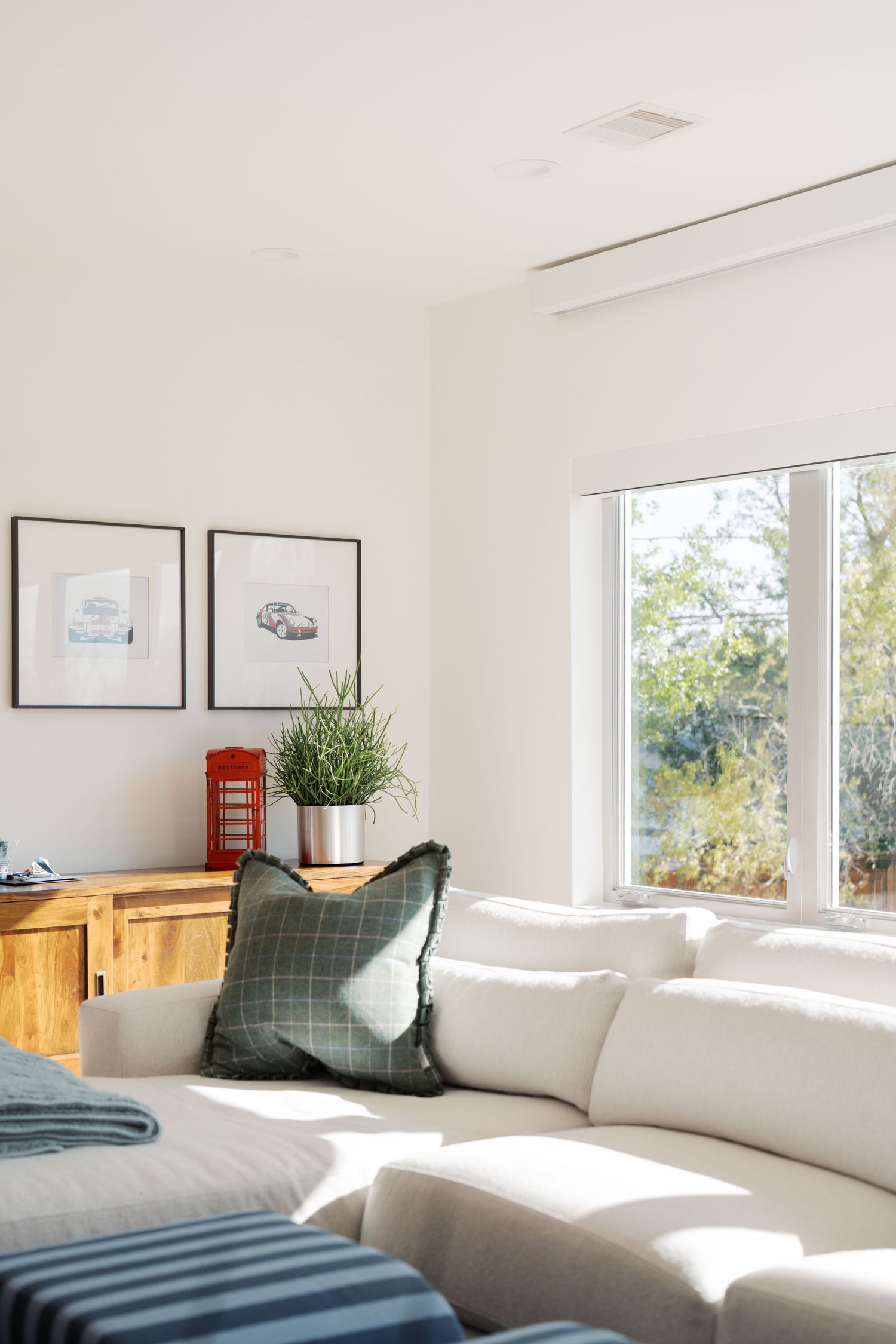 Bright modern living room with white sofa, green pillow, wood sideboard, framed art, and large window with natural light.