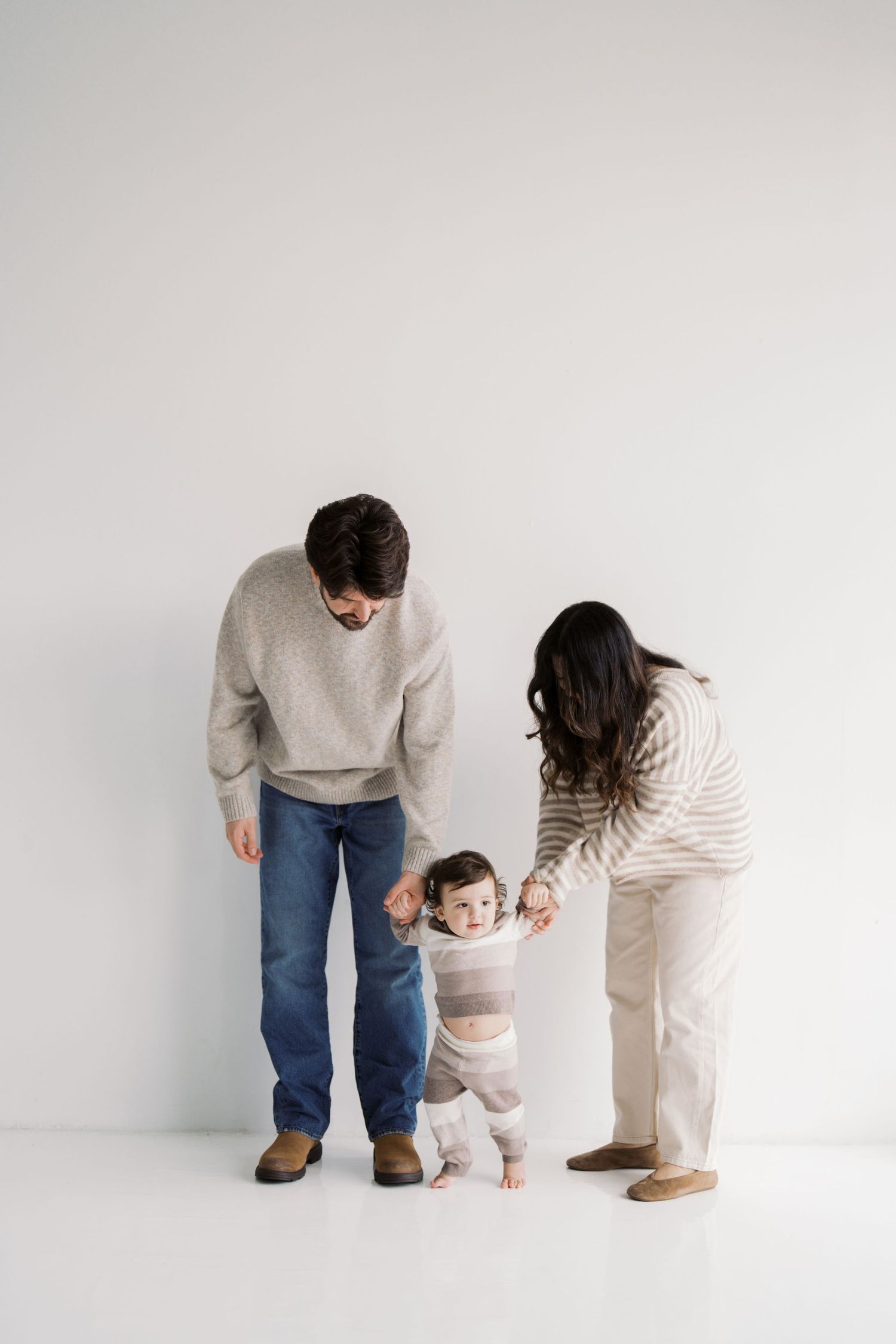 A family of three, a mother, father, and young child, standing together in a simple, minimalist setting.