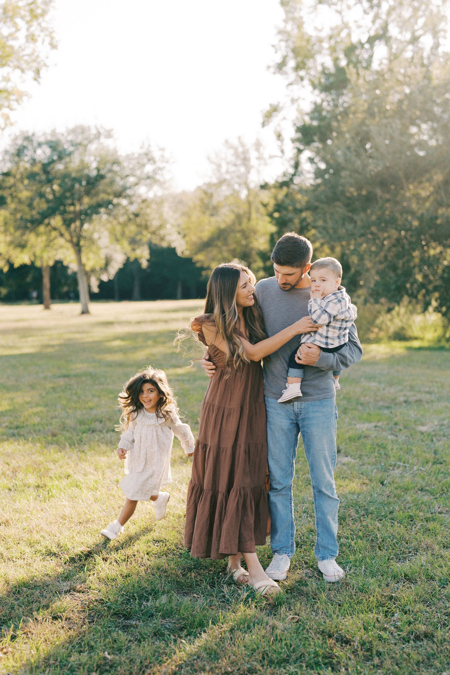 A family enjoys a playful moment together in a sunlit field during golden hour.
