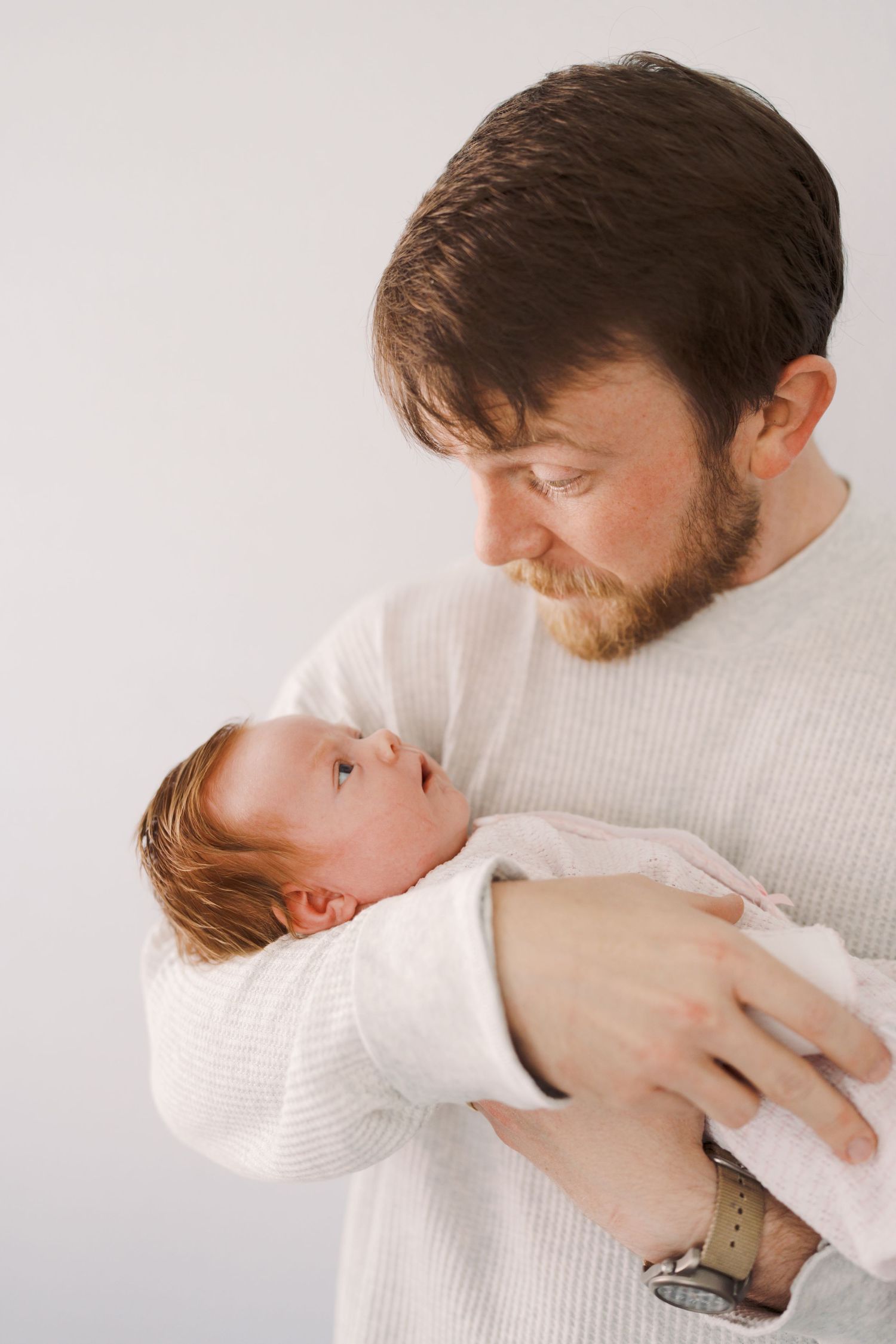 A close-up portrait of a man with a beard, tenderly holding a baby in his arms.