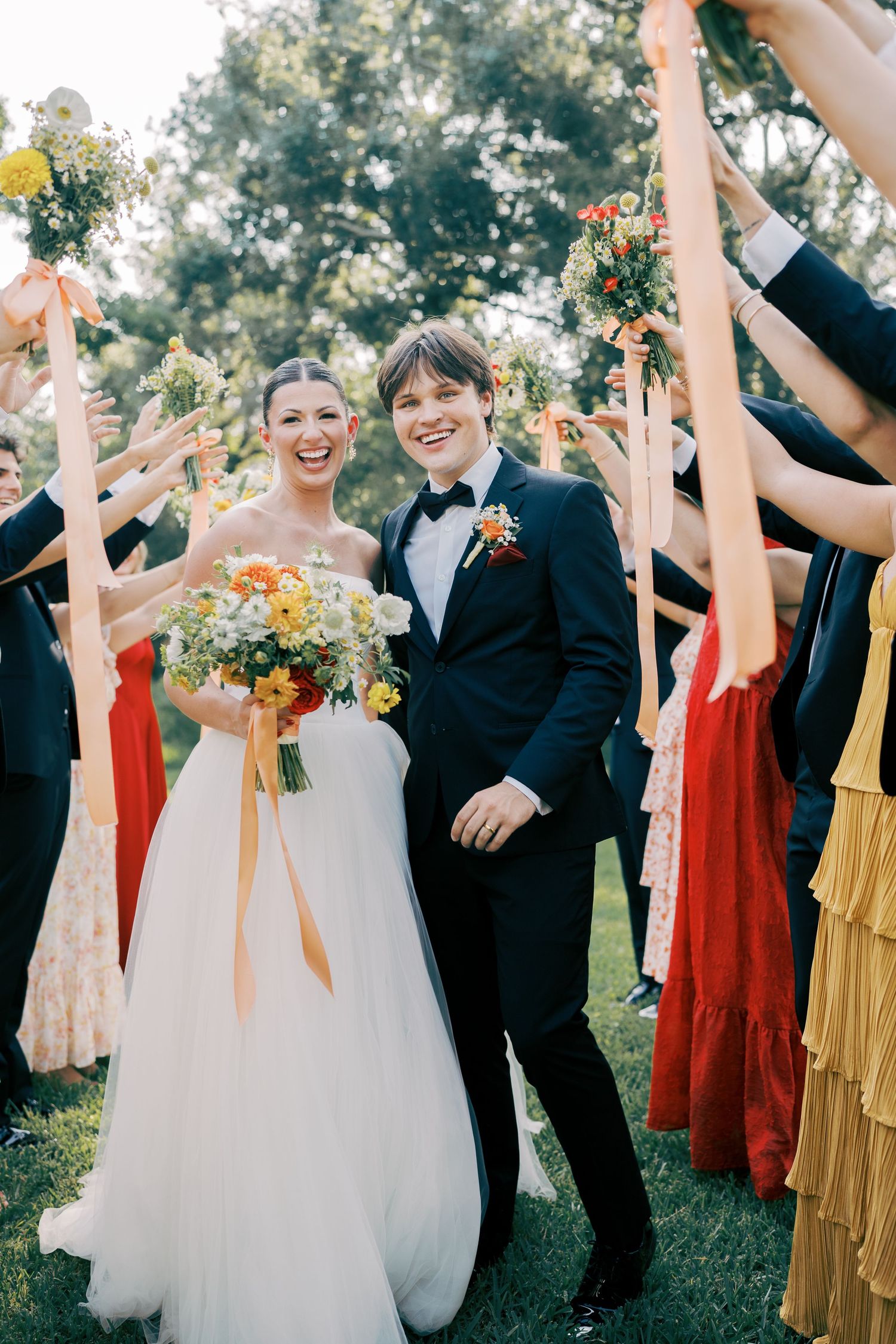 Wedding party celebrating outdoors in red and yellow dresses with joyful expressions.