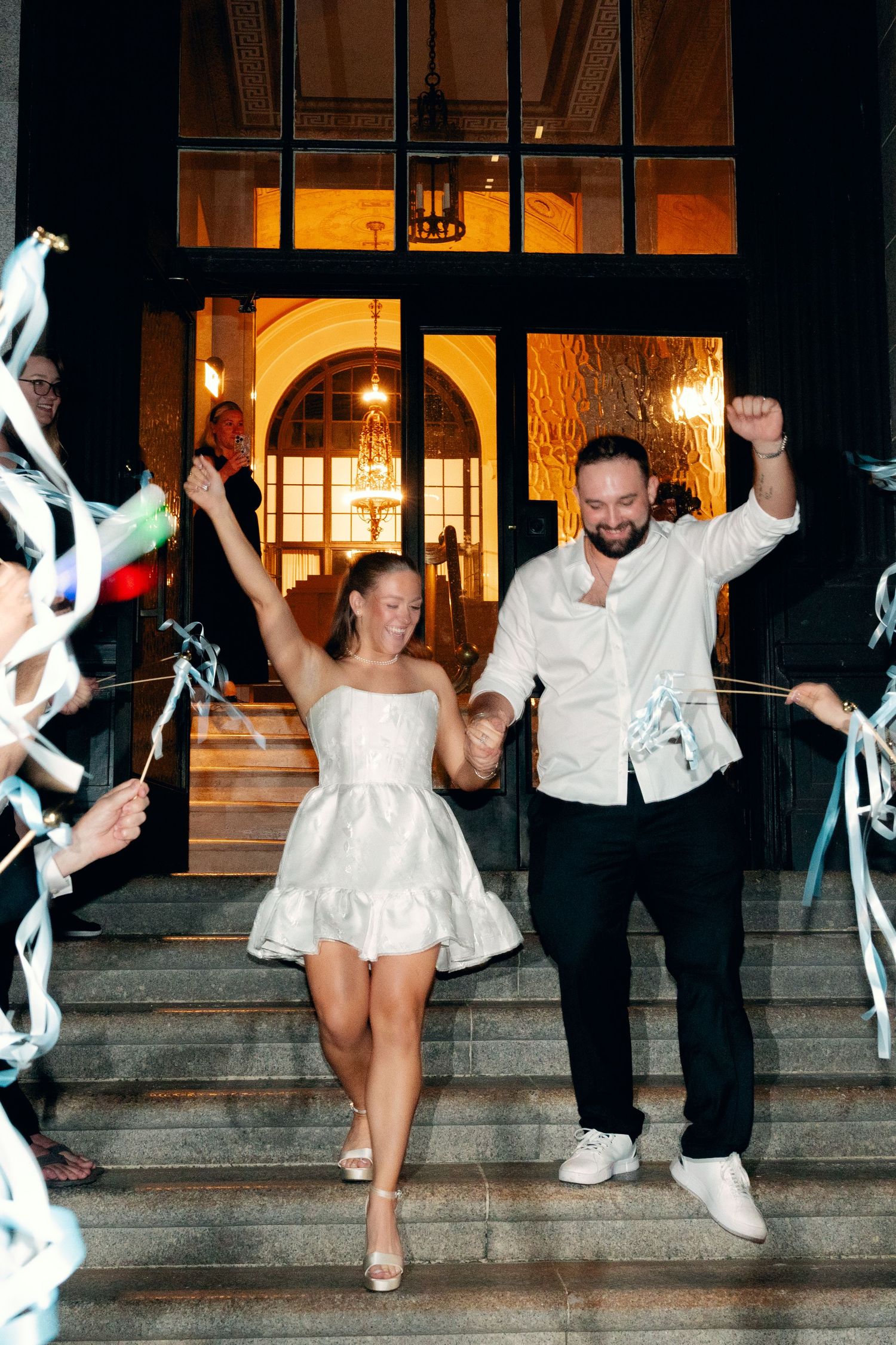 Wedding party jumping and celebrating on outdoor steps at night.