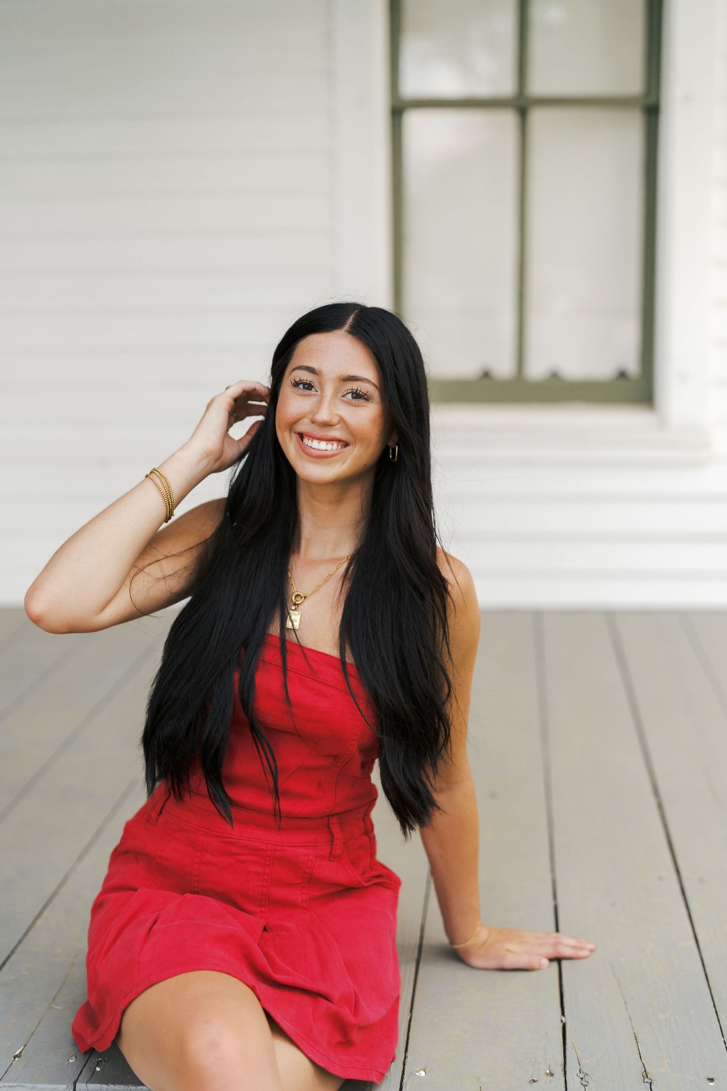 Portrait of person in red dress sitting on white porch with long dark hair.