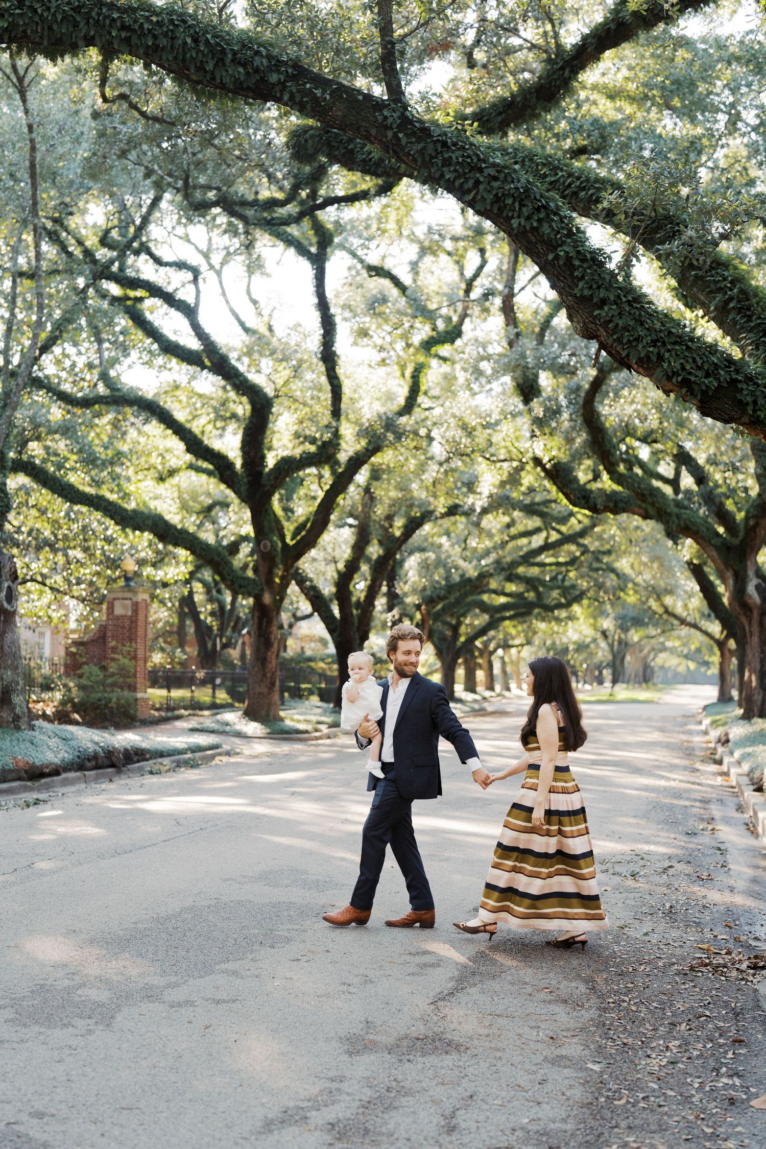 A couple dances together beneath towering oak trees with Spanish moss on a winding pathway in a romantic setting.