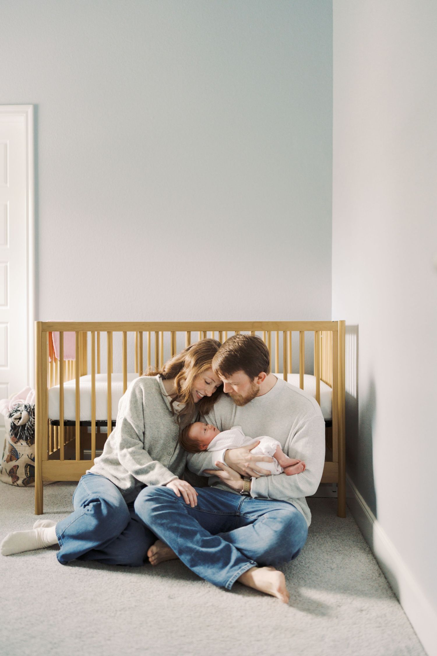 A couple sitting on the floor, embracing and looking at their newborn baby.
