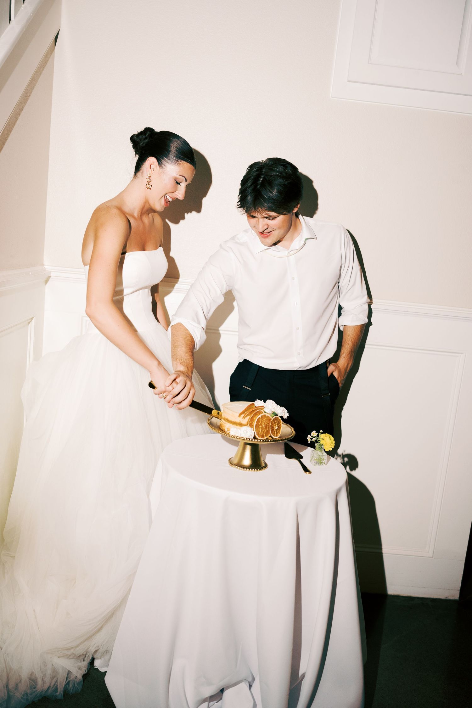Wedding couple cuts their cake together in an intimate indoor setting.
