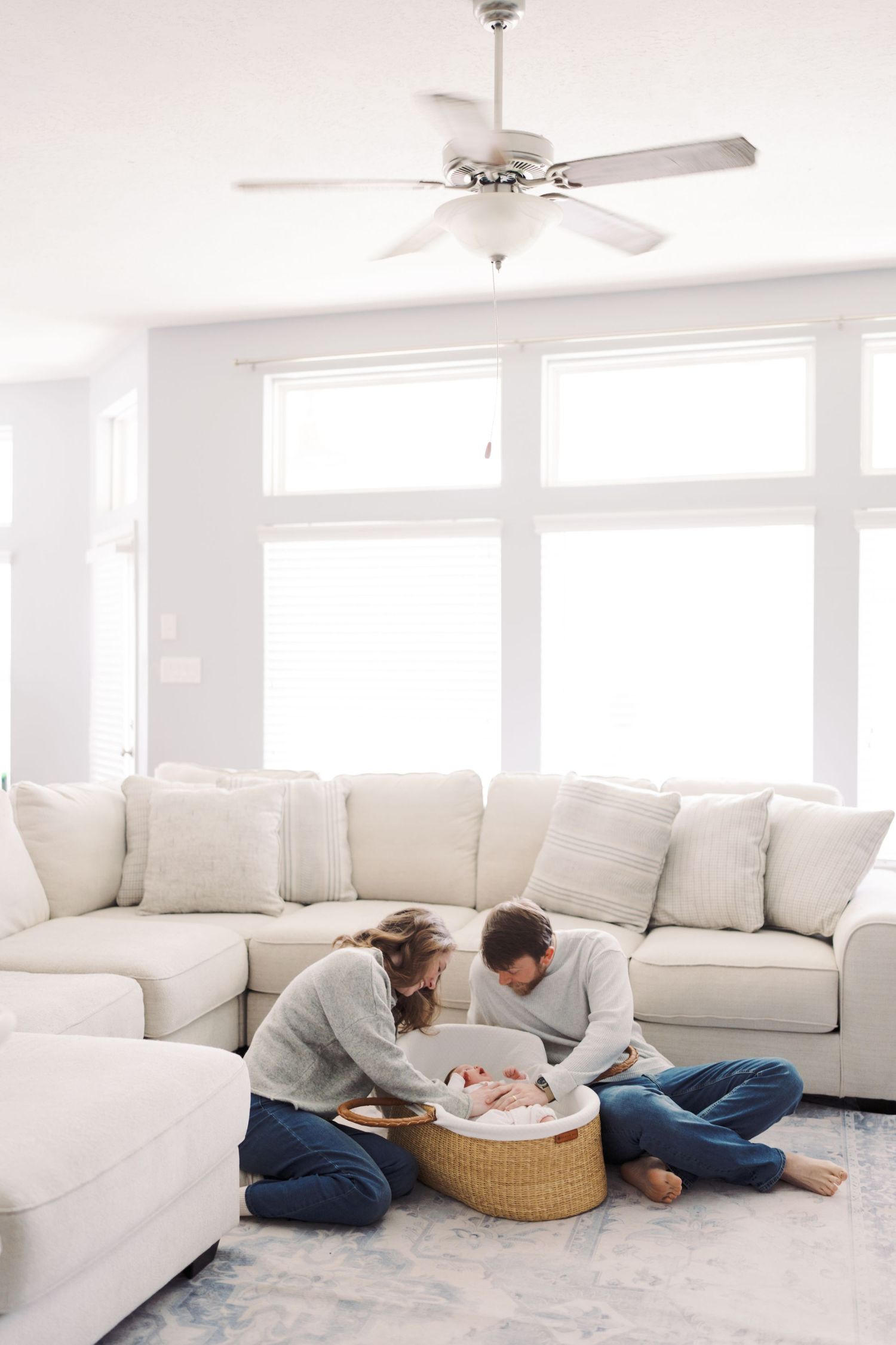 A family relaxing in a living room with a white couch and a ceiling fan overhead.