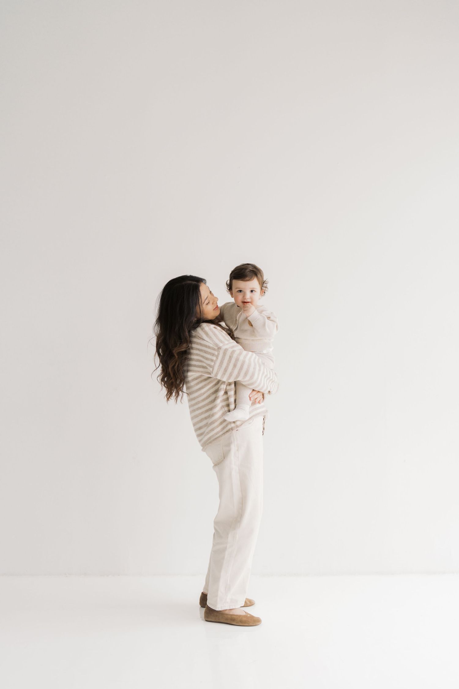 A woman in a beige sweater is holding a young child in her arms, creating a warm and affectionate scene.