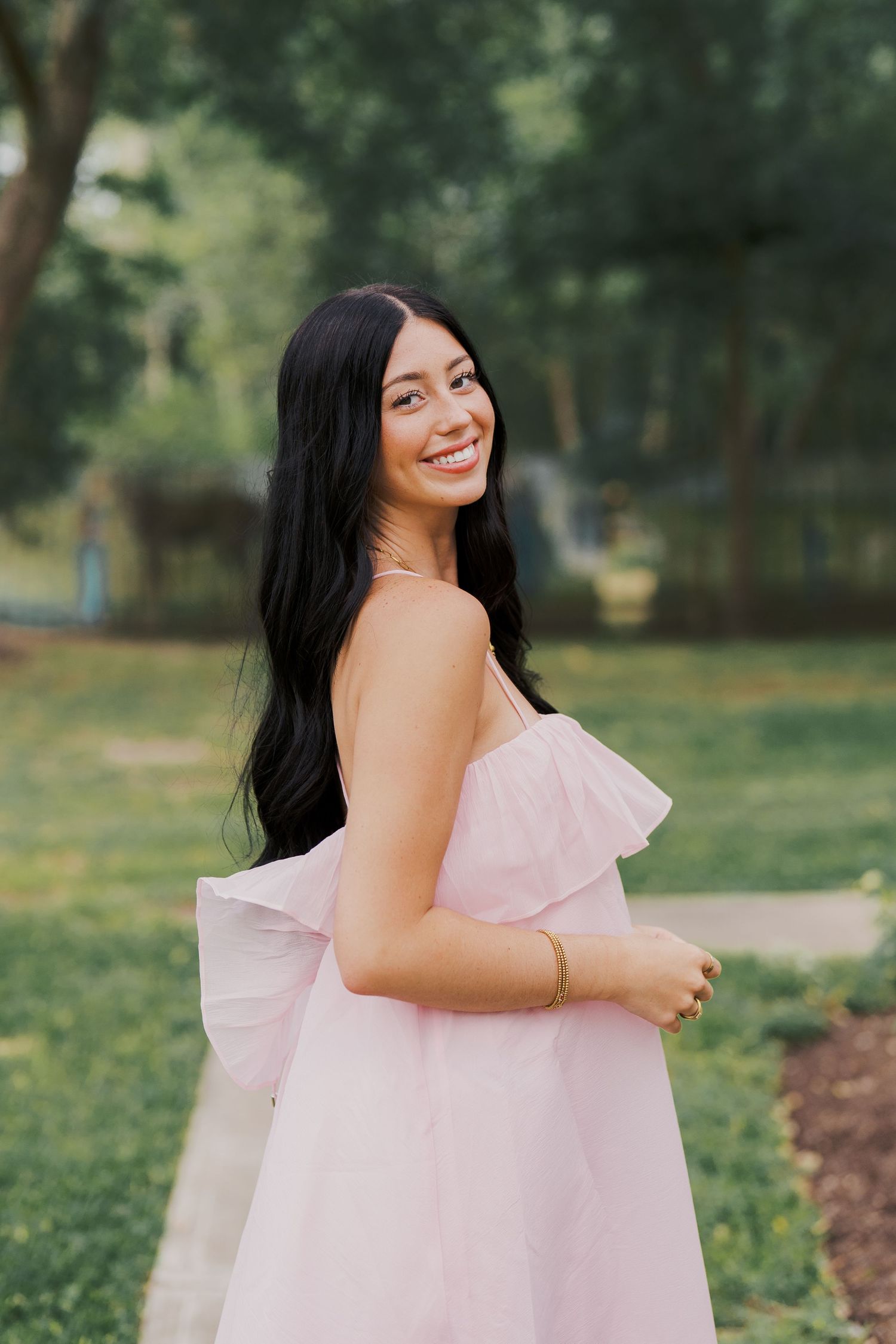 A woman in a pink dress smiles while standing in a garden setting.