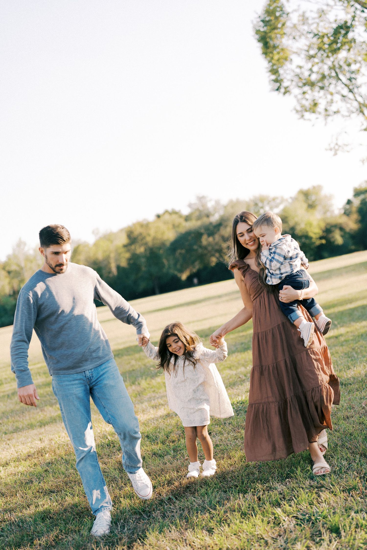 Family walking together and playing in a grassy field on a sunny afternoon.