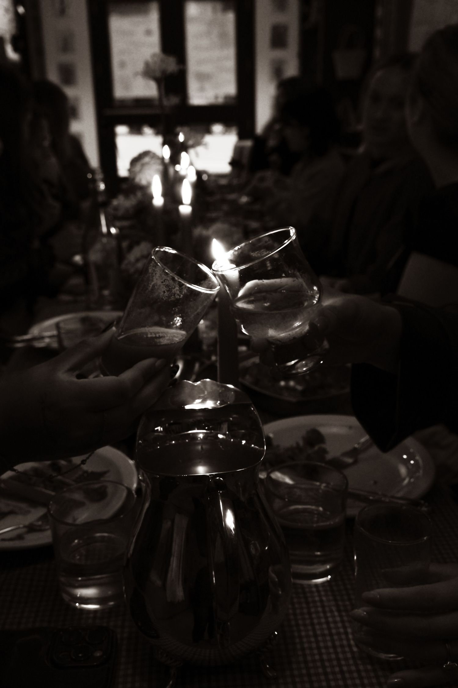 Dark moody black and white photo of guests clinking glasses over a candlelit dinner table.