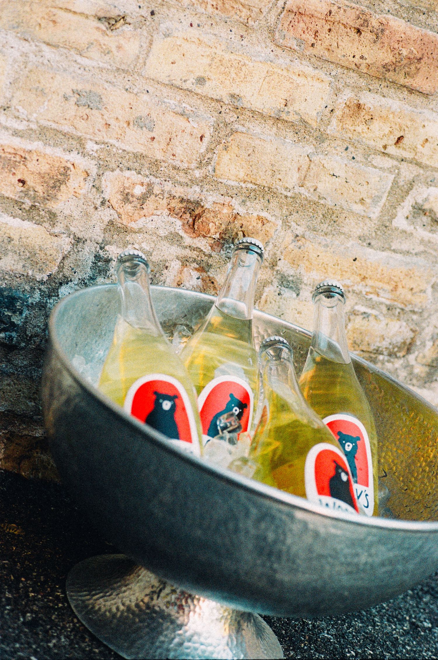 Glass bottles with bear labels chilling in ice-filled metal bucket against brick wall.