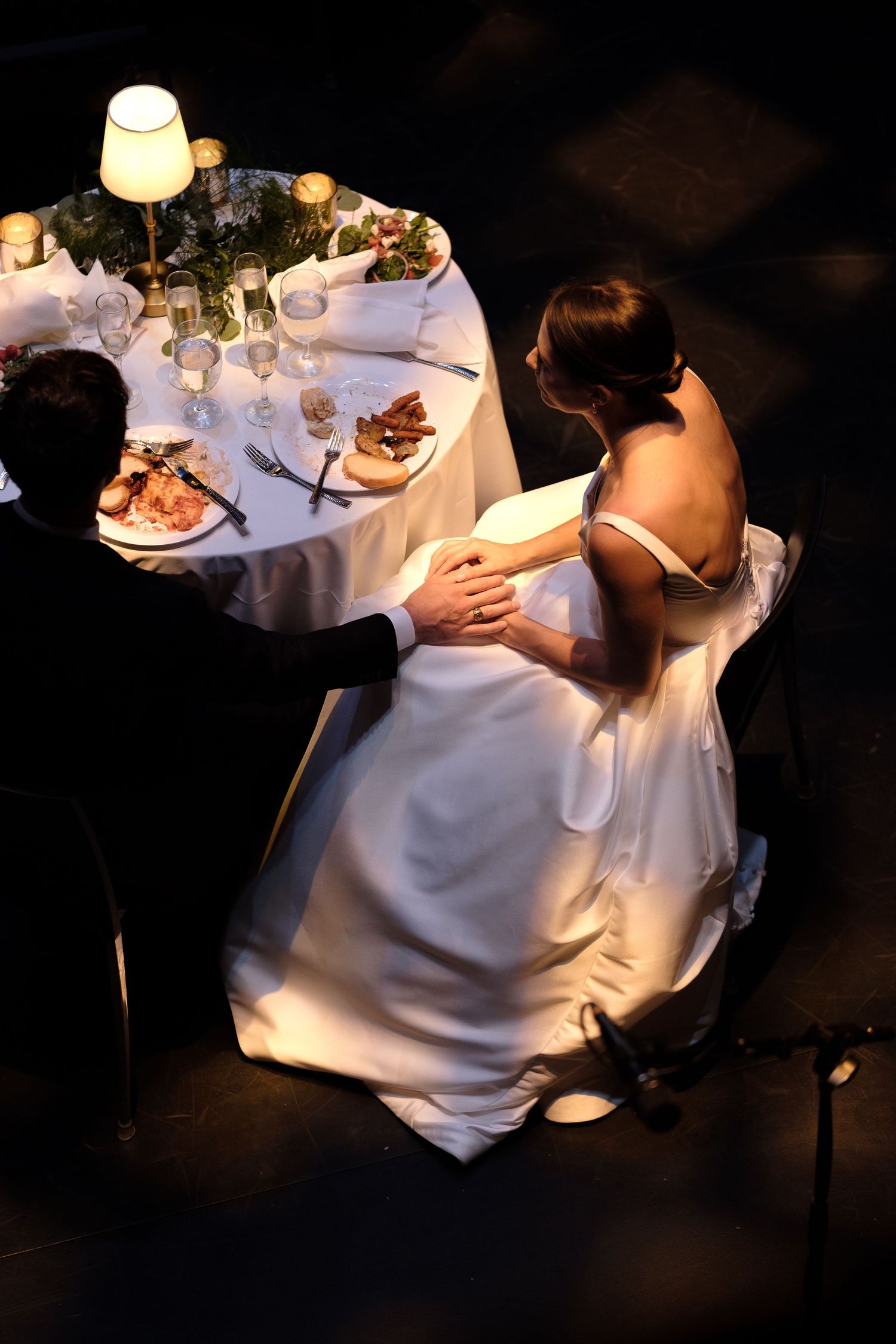 Aerial view of bride and groom seated at elegant wedding reception dinner table with candlelight.
