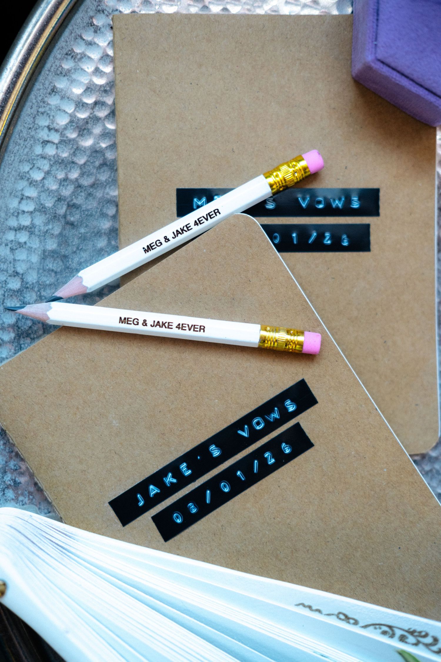 Custom wedding vow books with personalized pencils engraved with MEG & JAKE 4EVER on a decorative silver tray.
