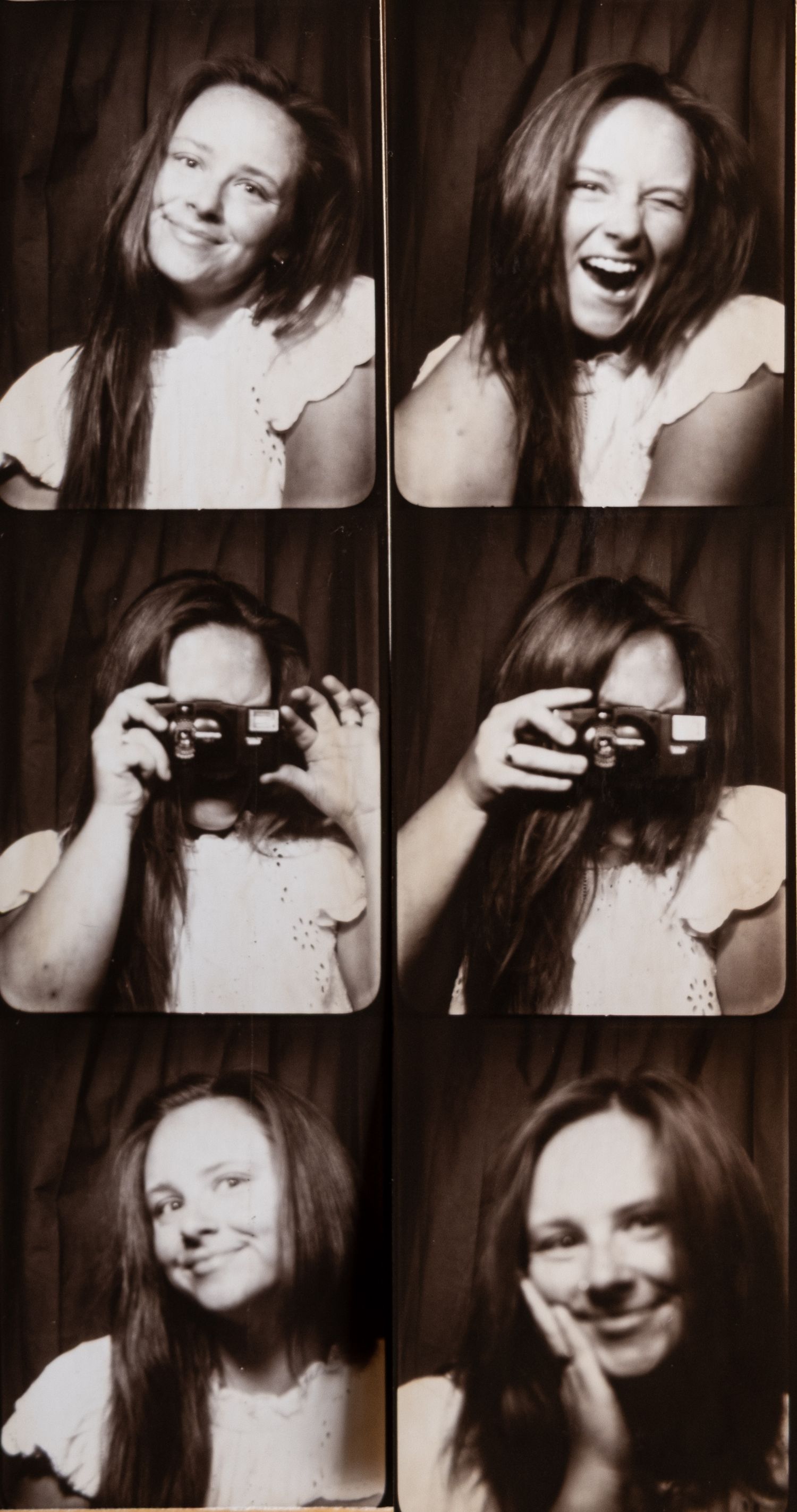 Black and white photo booth strip of a young woman with long hair laughing, holding a camera, and smiling playfully.