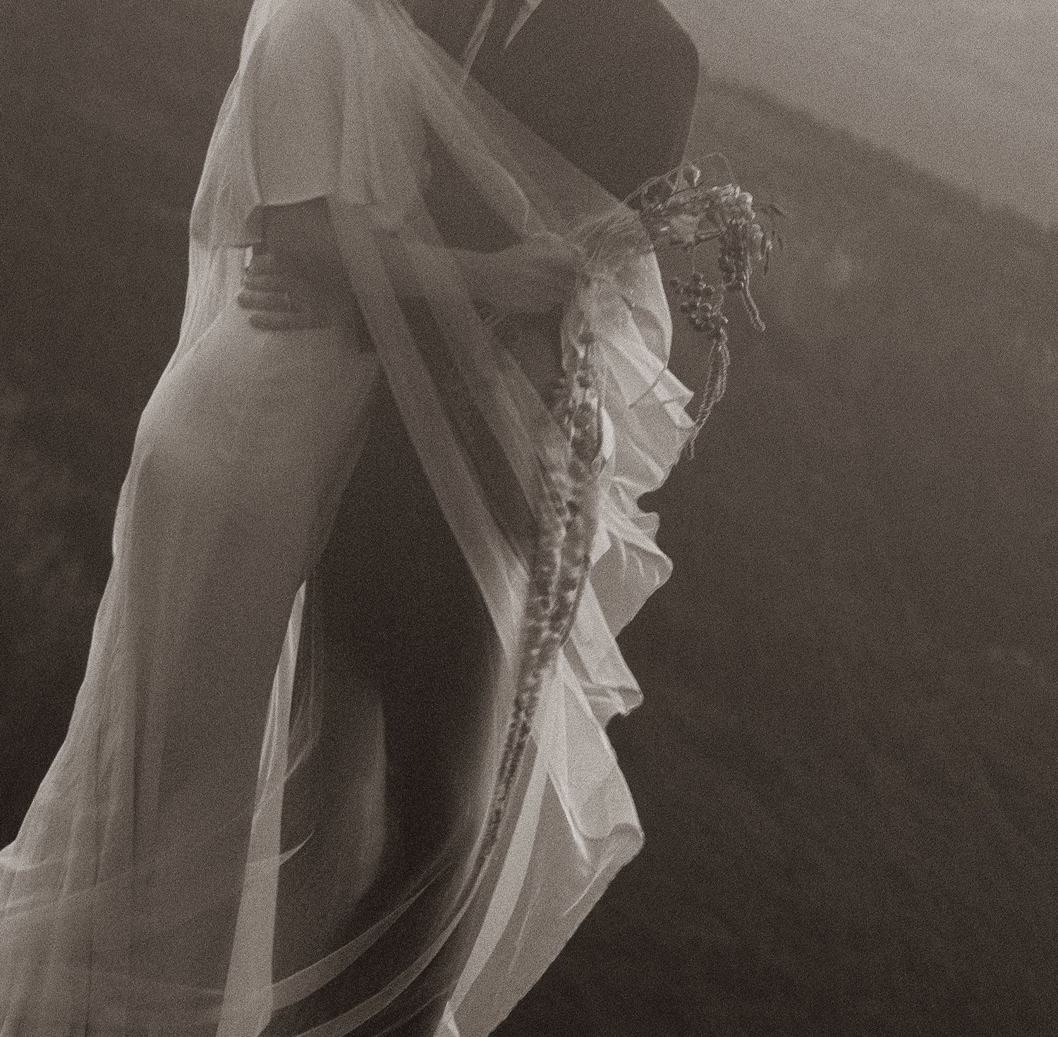 Romantic black and white maternity photo of a pregnant woman in a flowing white veil outdoors.