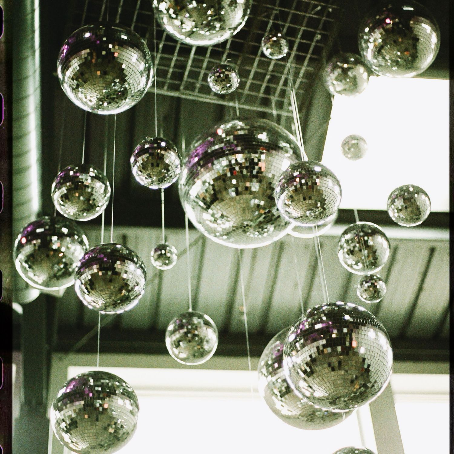 Multiple shimmering disco mirror balls hanging from a ceiling, reflecting light in a festive venue.