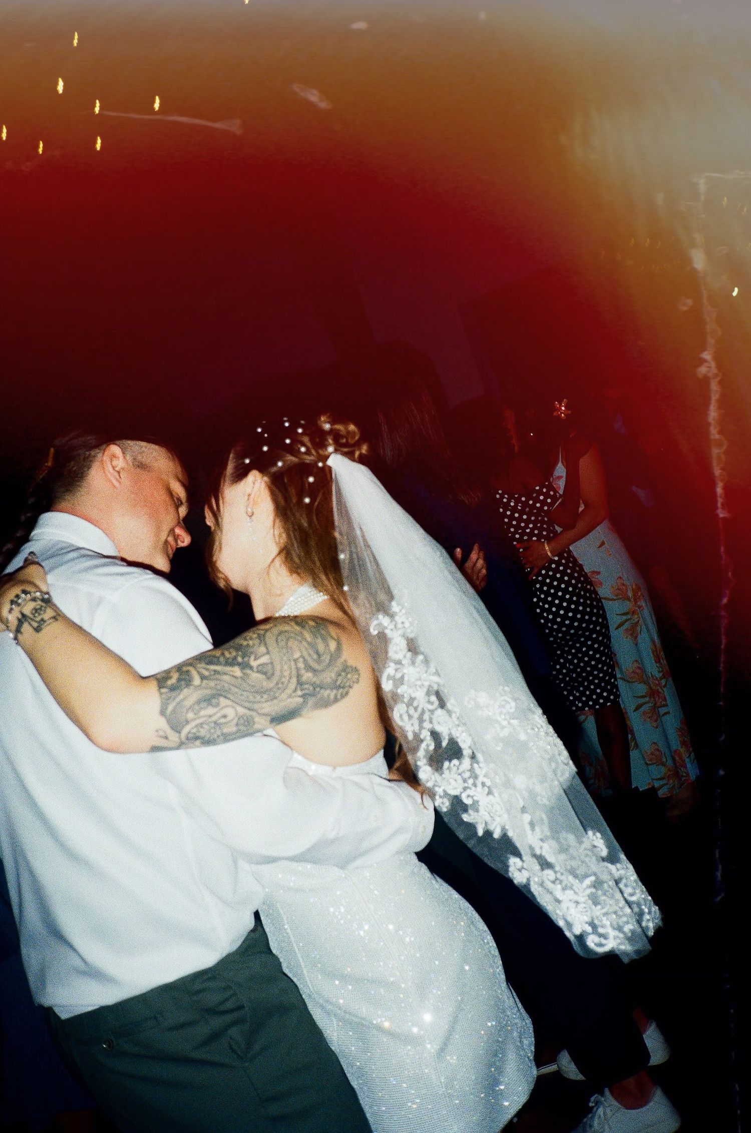 Bride and groom share first dance at wedding reception, bride wearing white gown and veil, groom with tattoo sleeve.