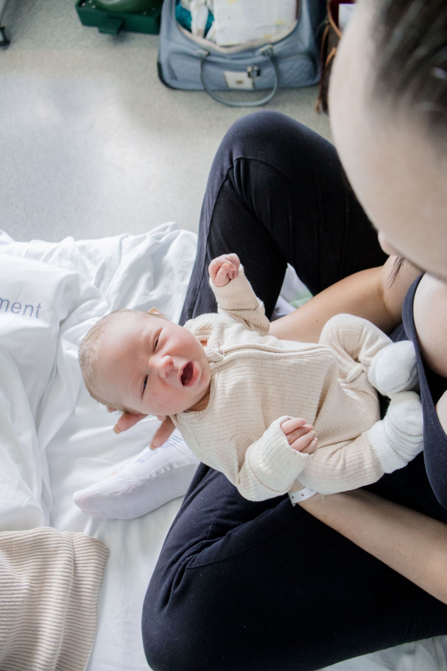 Happy baby in cream sweater lying on white bedding while being changed.