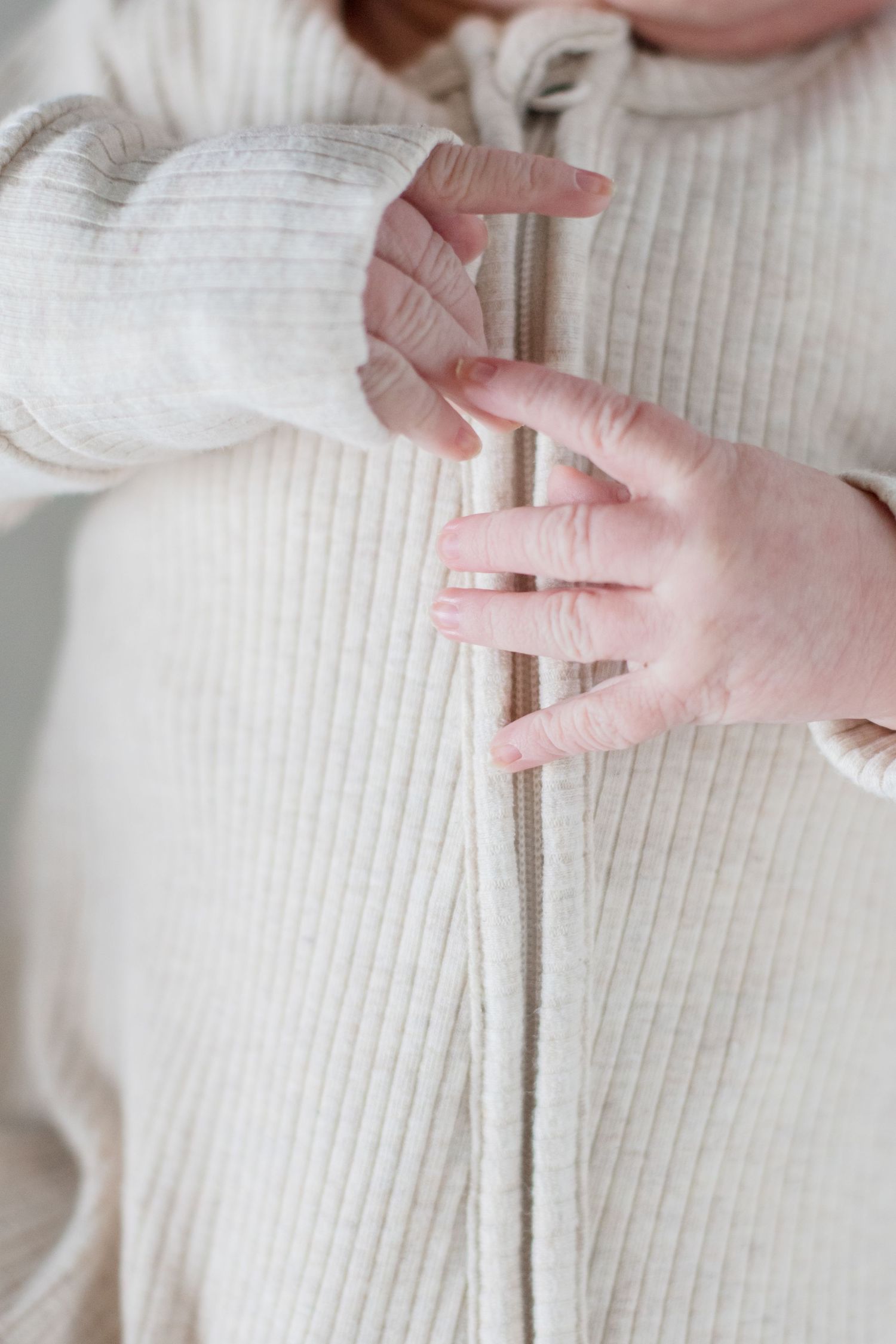 Close-up of small infant hands grasping white ribbed fabric.