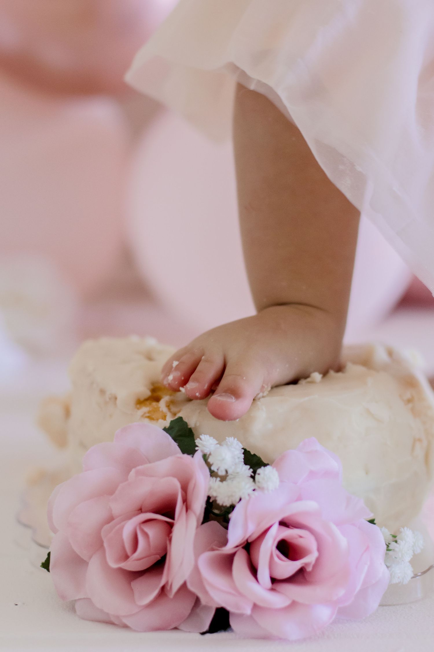Small hand reaching towards pink roses against white and cream party decorations.