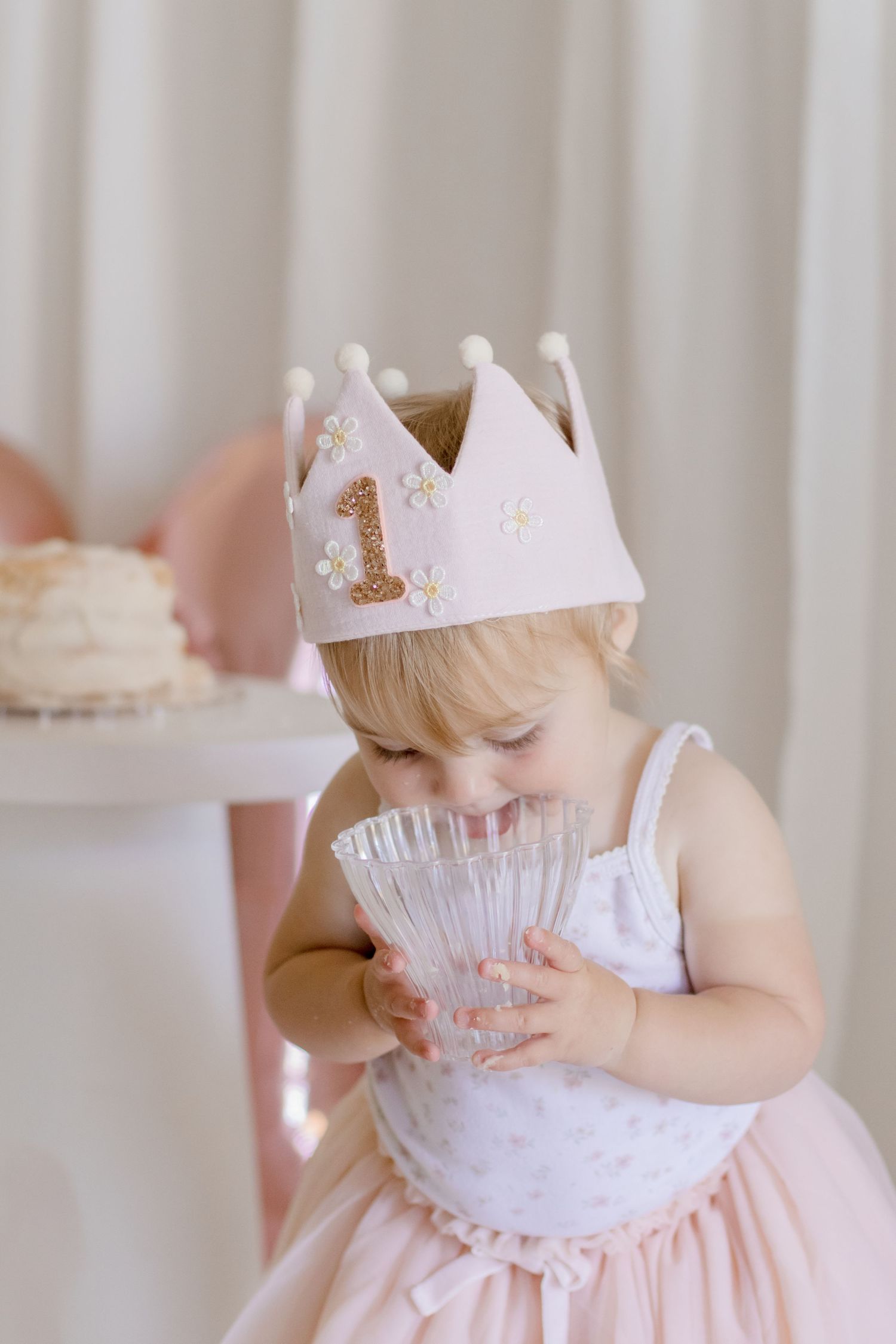 Small child in pink tulle dress and white crown examining crystal glass.
