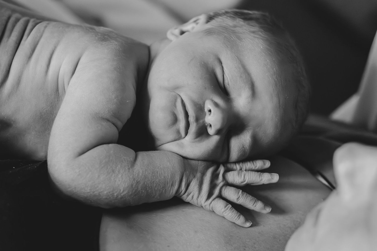 Black and white photo of a sleeping newborn baby resting peacefully on a parent's chest.