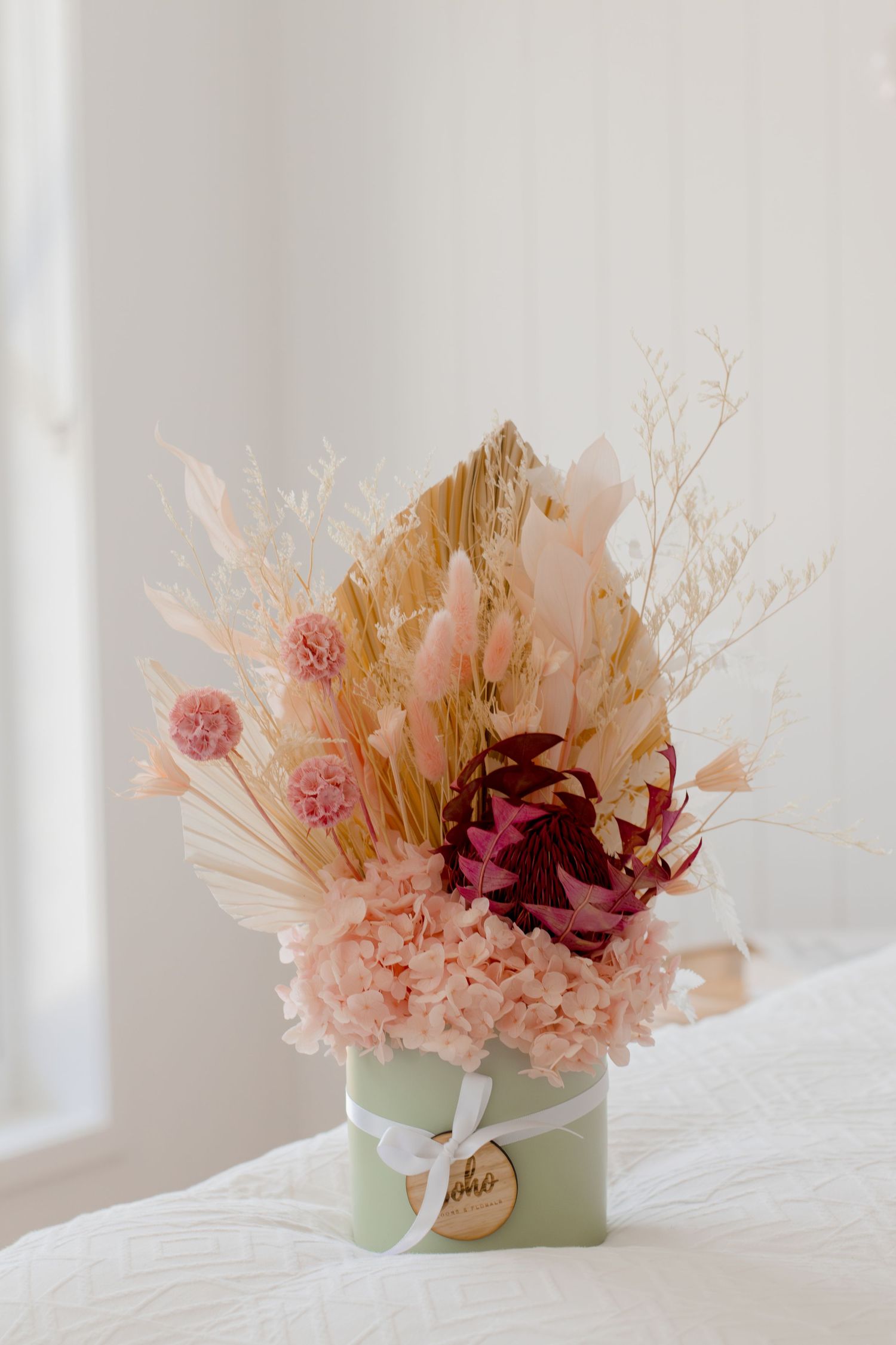 Elegant dried flower arrangement in a mint green box with pink hydrangeas, pampas grass, and burgundy blooms.